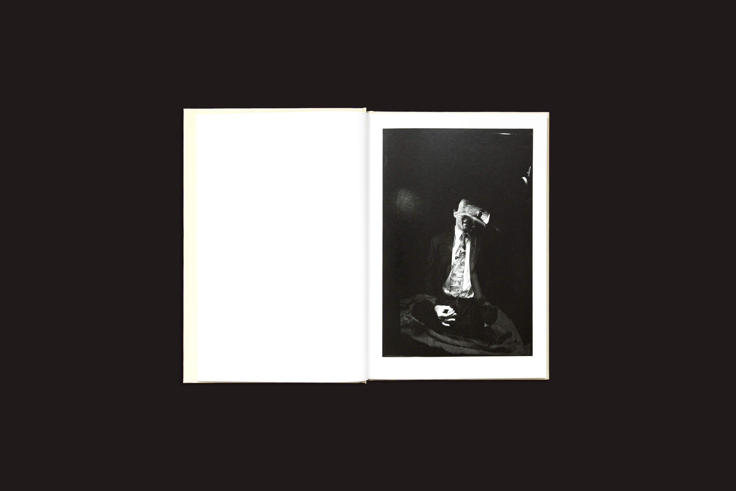 Uma página esquerda em branco contrasta com uma página direita exibindo uma imagem em preto e branco de "Cammie Toloui: 5 Dollars For 3 Minutes" de Void, retratando um objeto como uma estátua e um chapéu, colocados contra um fundo escuro, explorando sutilmente temas de masculinidade.