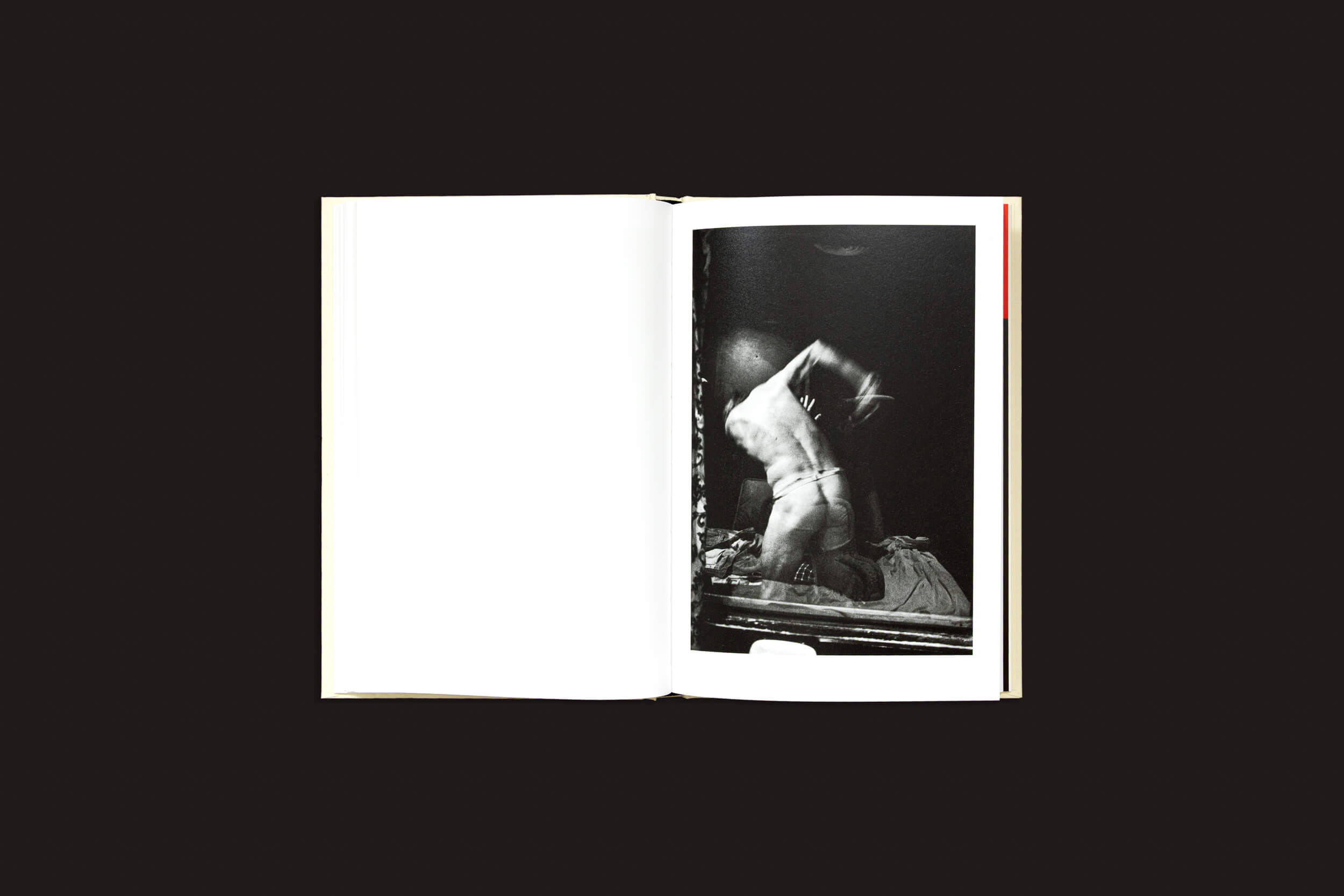 Um livro aberto, "Cammie Toloui: 5 Dólares por 3 Minutos", de Void, está sobre um fundo preto, exibindo uma foto monocromática, no estilo fotojornalismo, de uma figura em movimento, ajoelhada em uma cama com os braços levantados. A página da esquerda está em branco, enfatizando a fotografia vívida da direita.