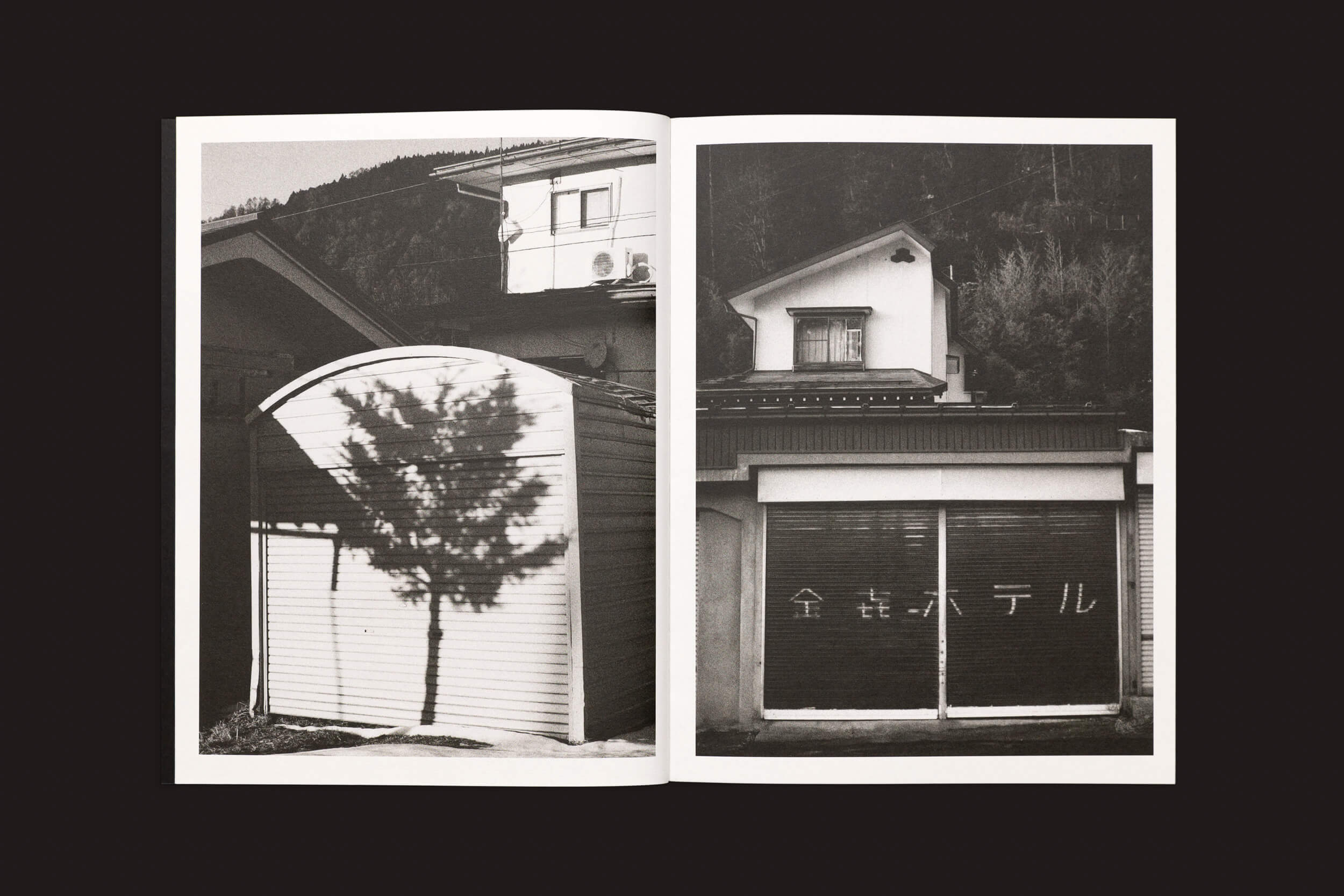 Uma imagem monocromática de Layla Motta: Ainda há um longo caminho até minha casa de Selo Turvo mostra a viagem de Layla pelo Japão. A sombra de uma árvore dança sobre um prédio à esquerda, enquanto a direita mostra a travessia emocional com veneziana fechada listrada adornada com texto em japonês.