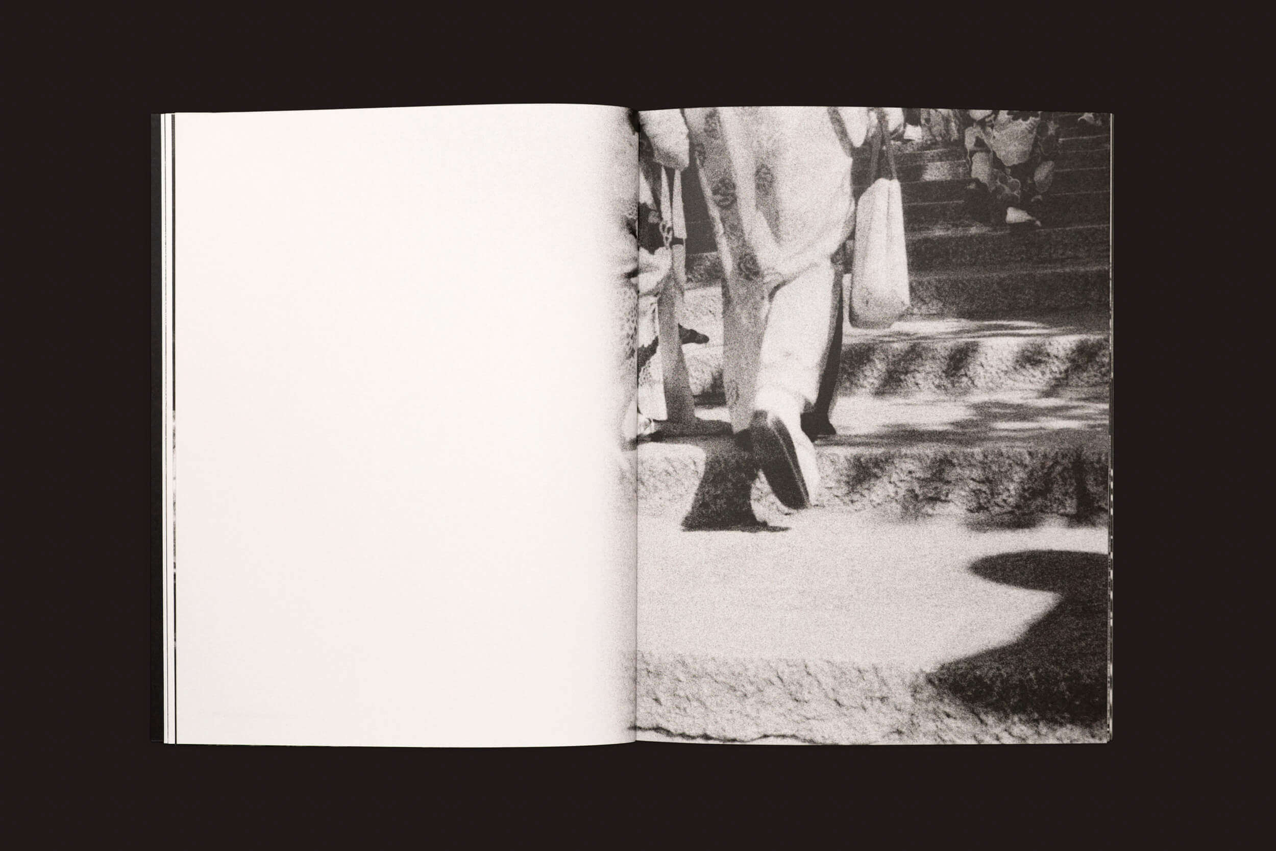 Um livro aberto, Layla Motta: Ainda há um longo caminho até minha casa, de Selo Turvo, mostra uma foto em preto e branco de pernas em movimento na página direita - uma homenagem à travessia emocional de Layla Motta. A página esquerda está em branco, convidando à reflexão.