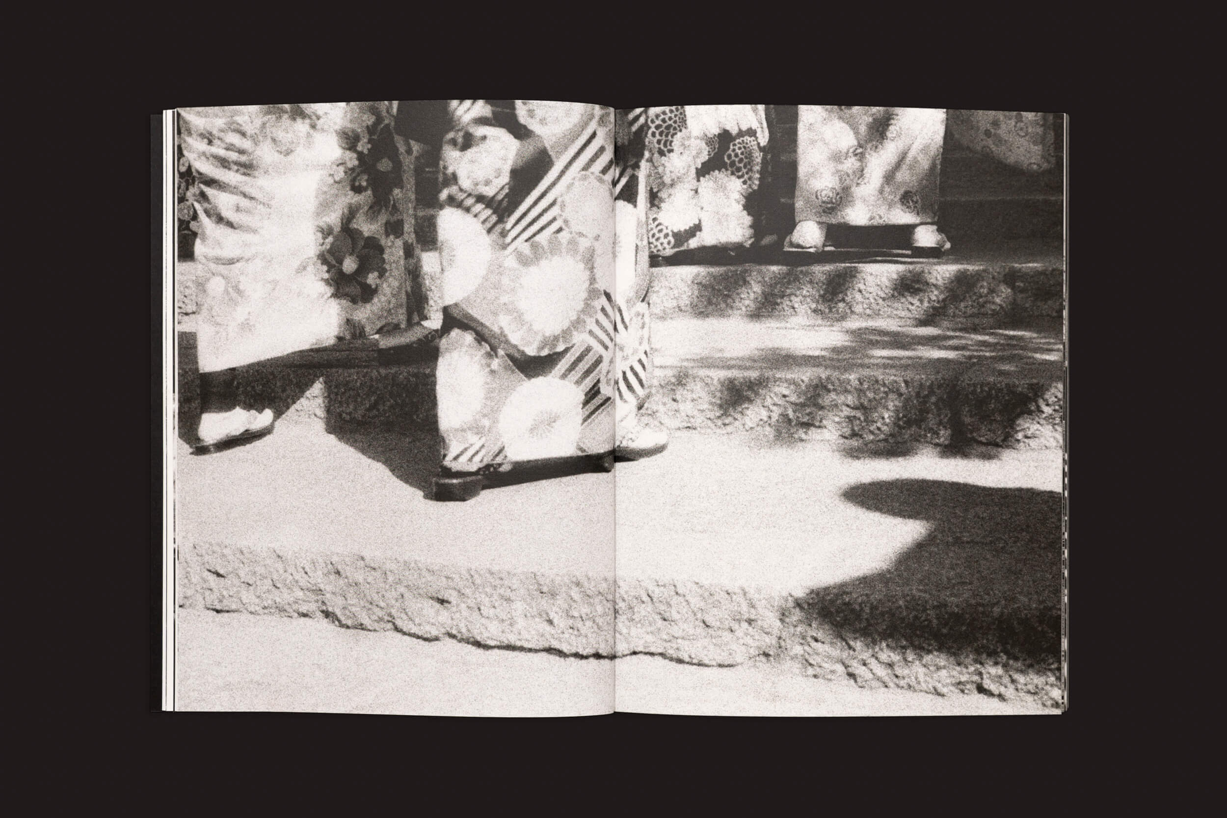 Em foto monocromática de Layla Motta: Ainda há um longo caminho até minha casa, de Selo Turvo, pessoas em trajes tradicionais japoneses sobem degraus de pedra. O foco nas roupas estampadas e nas sandálias capta uma viagem emocional, travessia emocional, em meio às sombras projetadas nos degraus.