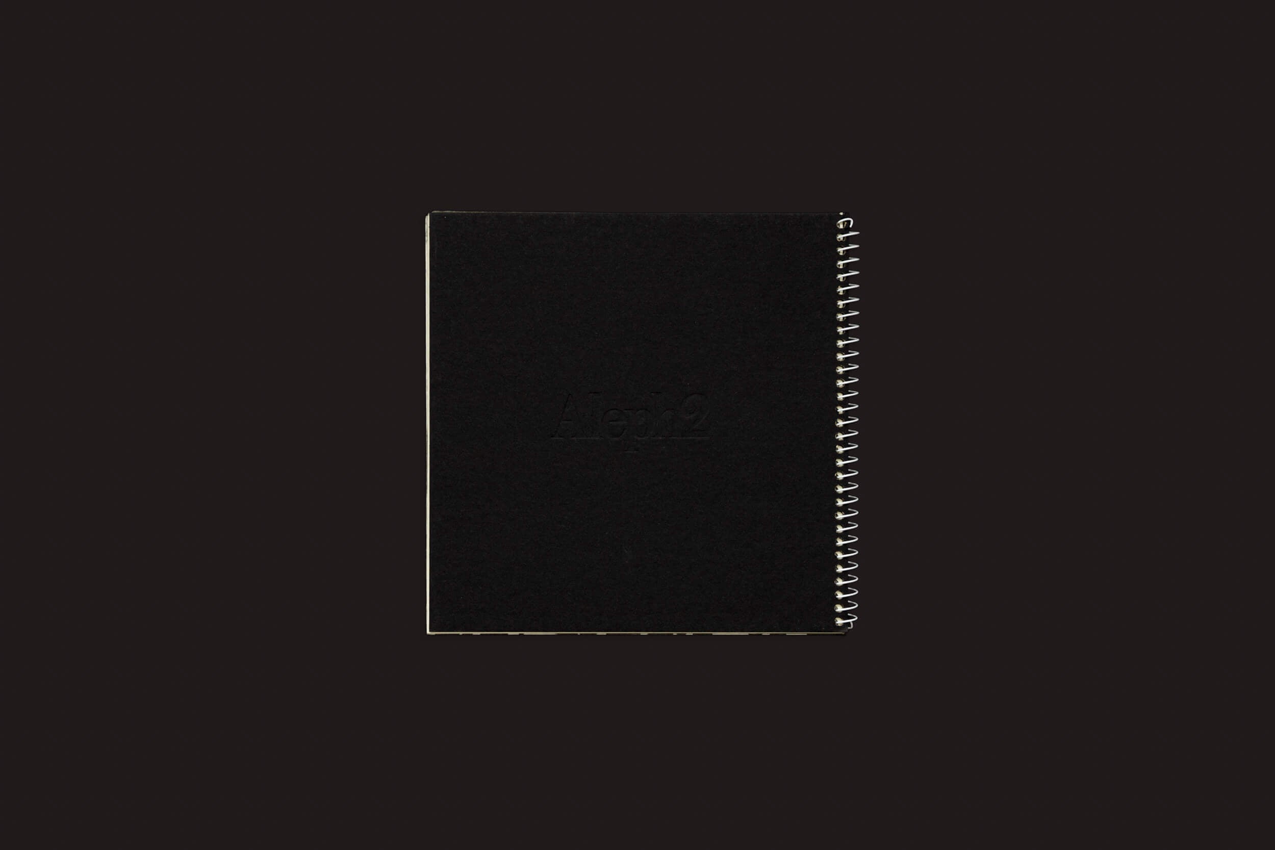 Um caderno elegante, preto, encadernado em espiral e com capa escura, tão misterioso quanto o Juan Manuel Lara: Aleph-2 da SED Editorial, repousa sobre um fundo preto simples.