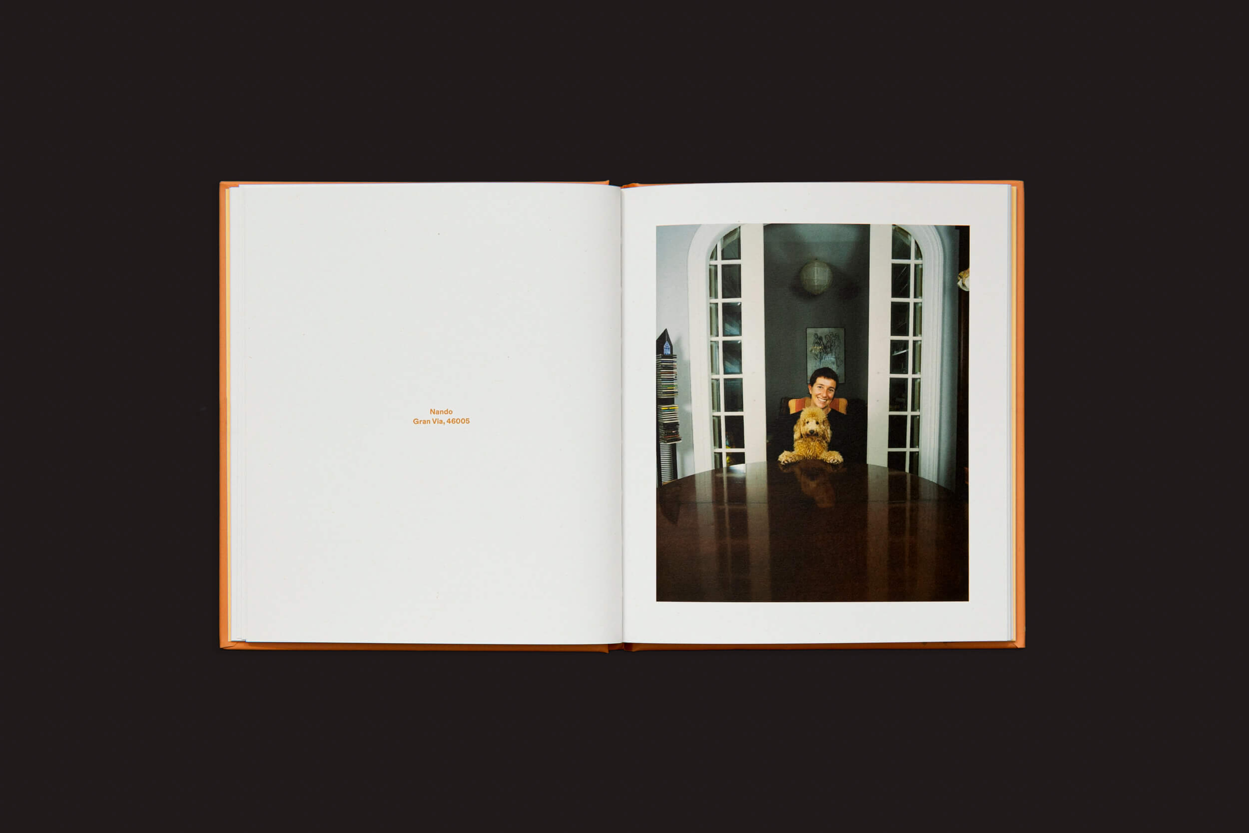 Um livro aberto sobre uma superfície escura mostra uma foto de alguém em uma mesa de madeira com um Poodle Apricot. A página da esquerda apresenta o texto Bacio e Osvaldo AGOSTO em um fundo claro, capturando dinâmica social e imitação. Produto: Laura Leal: Poodle Apricot da Handshake.