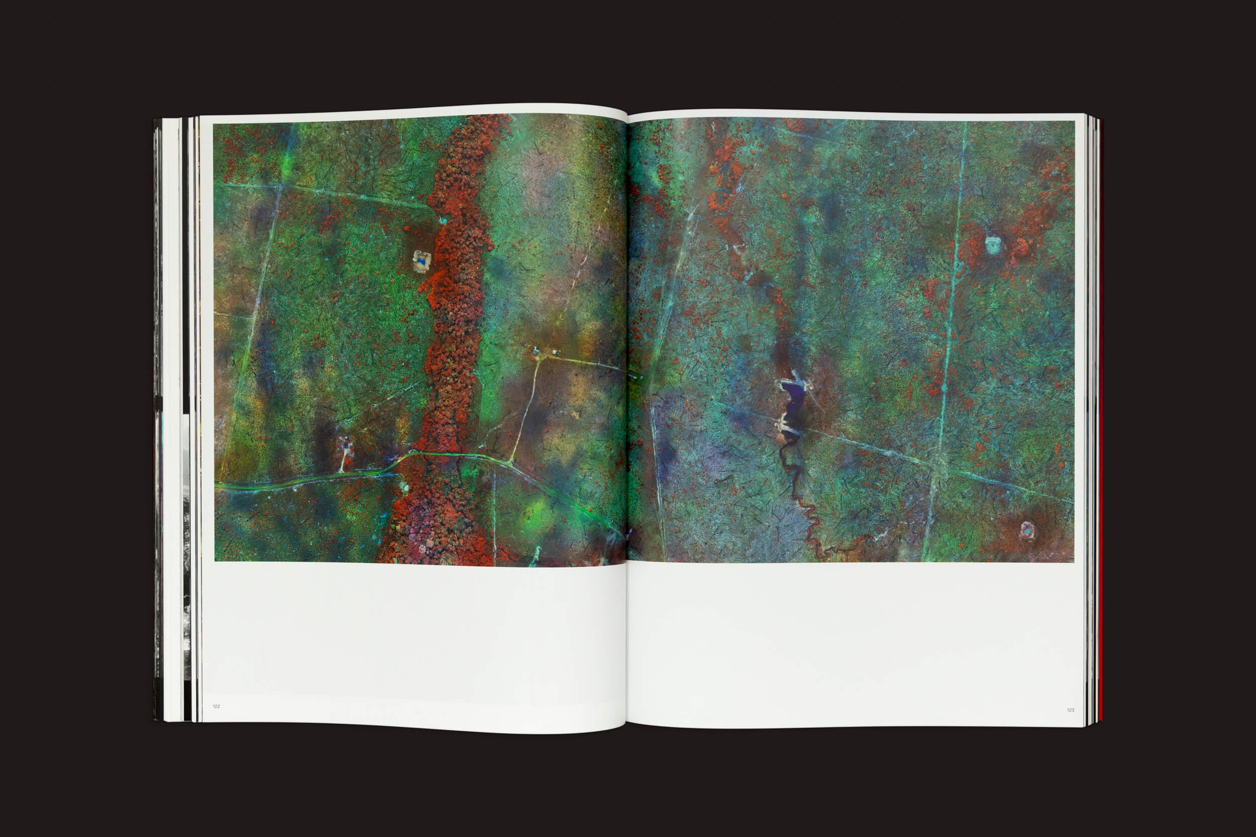 Richard Mosse: Broken Spectre, de Loose Joints, exibe páginas abertas de paisagens aéreas em verde e vermelho, com linhas e padrões ilustrando alterações climáticas. Margens brancas largas cercam as imagens, enquanto um fundo escuro acentua a presença do livro.