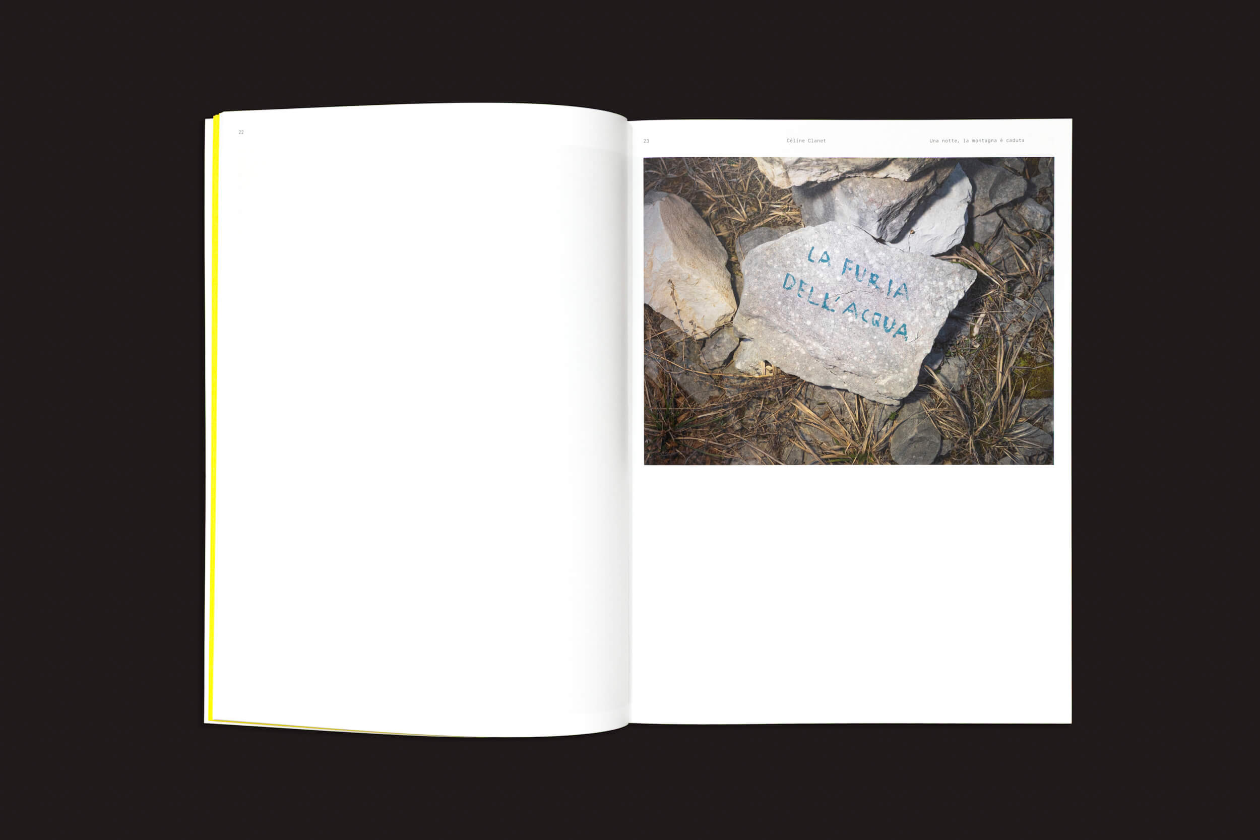 Uma cópia aberta de CALAMITA/À – Uma investigação sobre a catástrofe de Vajont: v/a, da Fw:Books, revela uma foto de uma pedra com a inscrição "LA FUERA DELLA ACQUA", evocando o desastre de Vajont, na página direita, em meio a grama seca e pedras; a página esquerda está em branco.