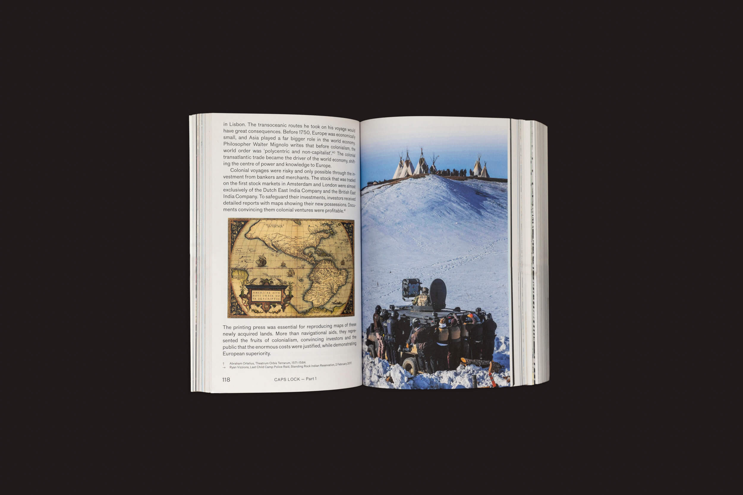 Um livro aberto, "Caps Lock", de Ruben Pater, de Valiz, apresenta texto e um mapa antigo na página esquerda, com uma foto de uma paisagem nevada na direita mostrando pessoas em trajes tradicionais perto de tipis ao lado de uma equipe de filmagem envolvida em práticas socialmente conscientes.