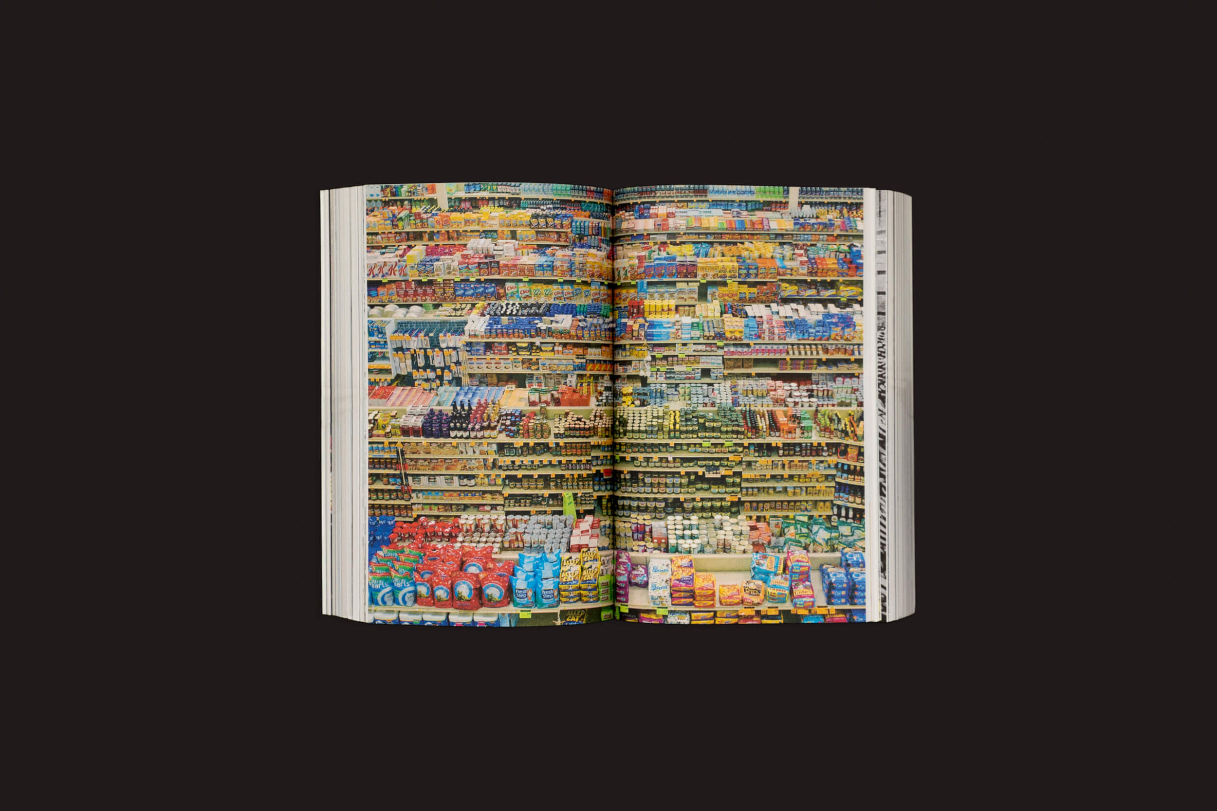 Um livro aberto, "Caps Lock - Como o capitalismo tomou conta do design gráfico e como escapar dele", de Ruben Pater (Valiz), revela uma foto vibrante de um supermercado, mostrando a interação colorida do design gráfico e do capitalismo contra um fundo preto.