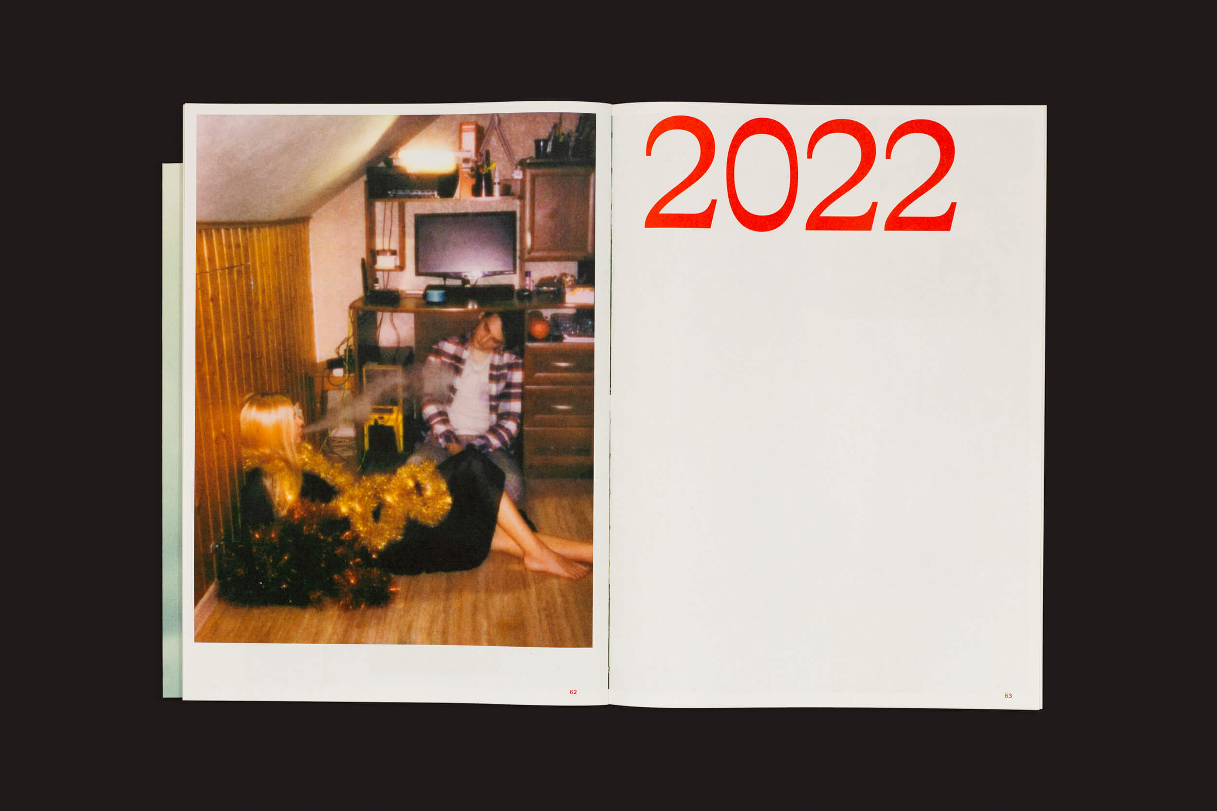 Um livro aberto intitulado Toma Gerzha: Control Refresh por The Eriskay Connection exibe uma foto borrada de uma pequena sala com Toma Gerzha e outra pessoa perto de uma árvore decorada e TV, ecoando sussurros de propaganda de guerra. A página oposta está em branco, exceto pelos grandes números vermelhos 2022 no topo.