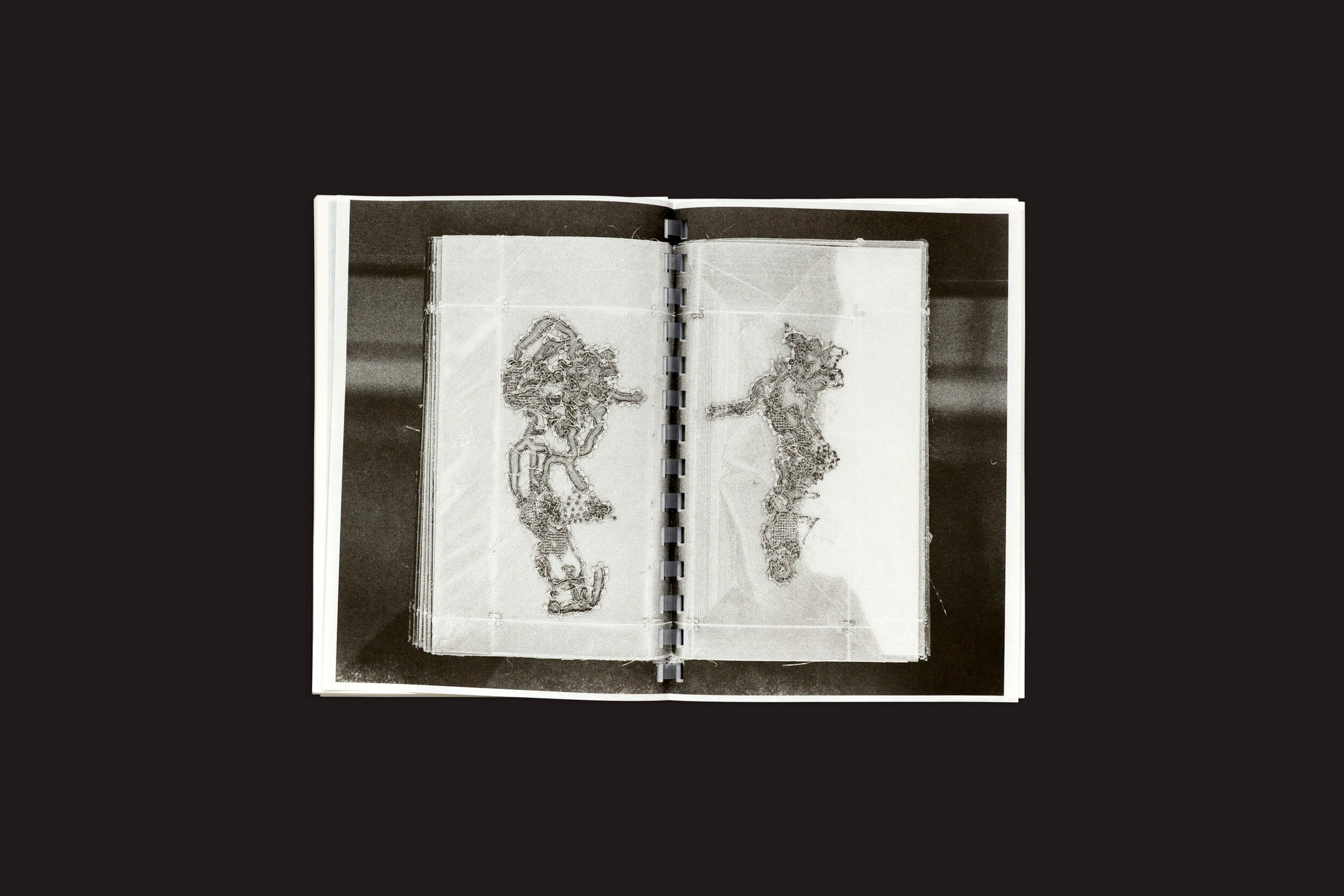 O Darius Ou: Corpus da Temporary Press, um livro aberto encadernado em espiral, é exibido contra um fundo escuro. Suas páginas translúcidas apresentam padrões abstratos, semelhantes a rendas, com designs intrincados que refletem o talento artístico do designer gráfico Darius Ou.