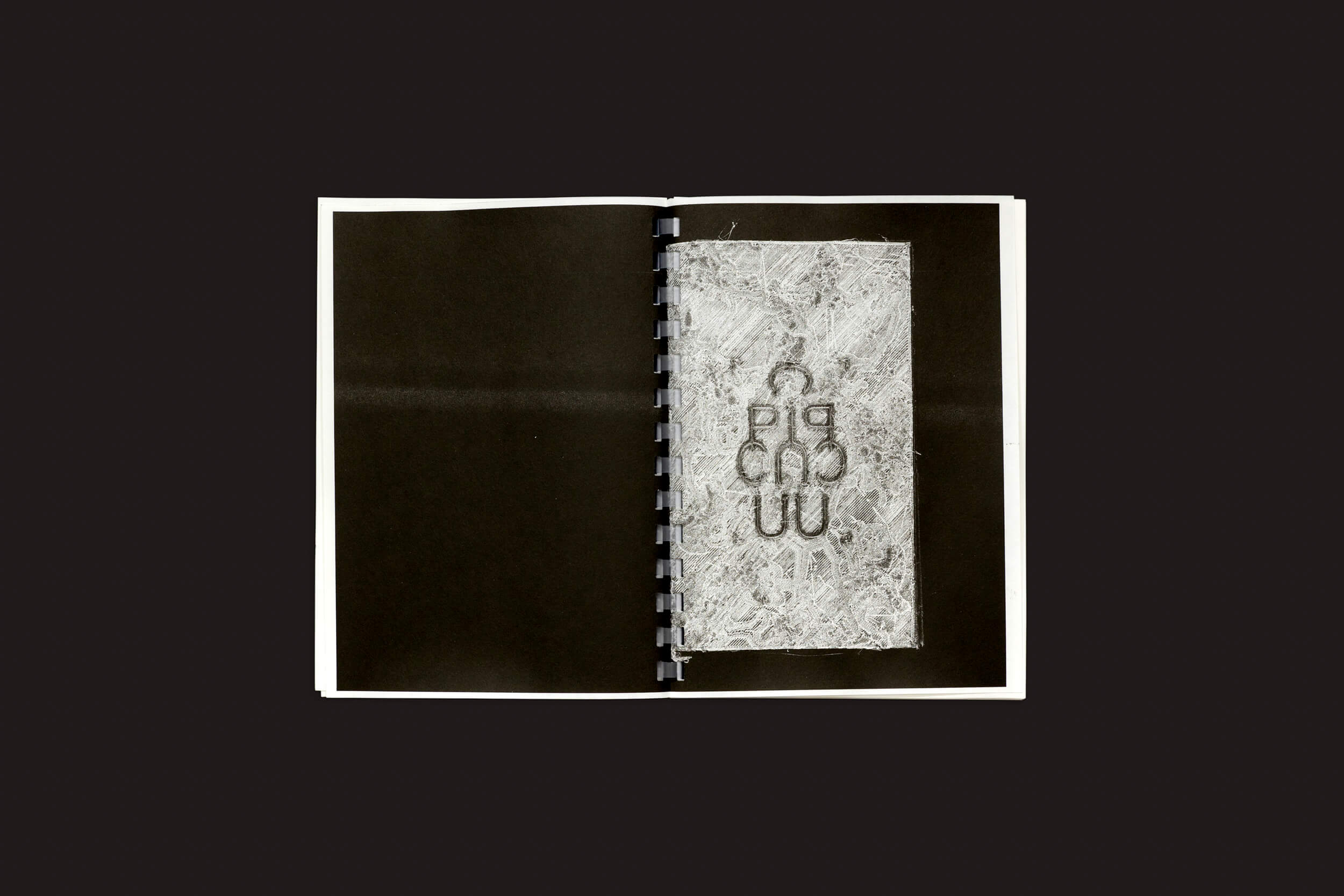 Em um fundo escuro está Darius Ou: Corpus, um livro aberto encadernado em espiral pela Temporary Press. A página da esquerda está em branco, enquanto a da direita apresenta padrões abstratos e formas geométricas, apresentando a visão artística do designer gráfico Darius Ou.