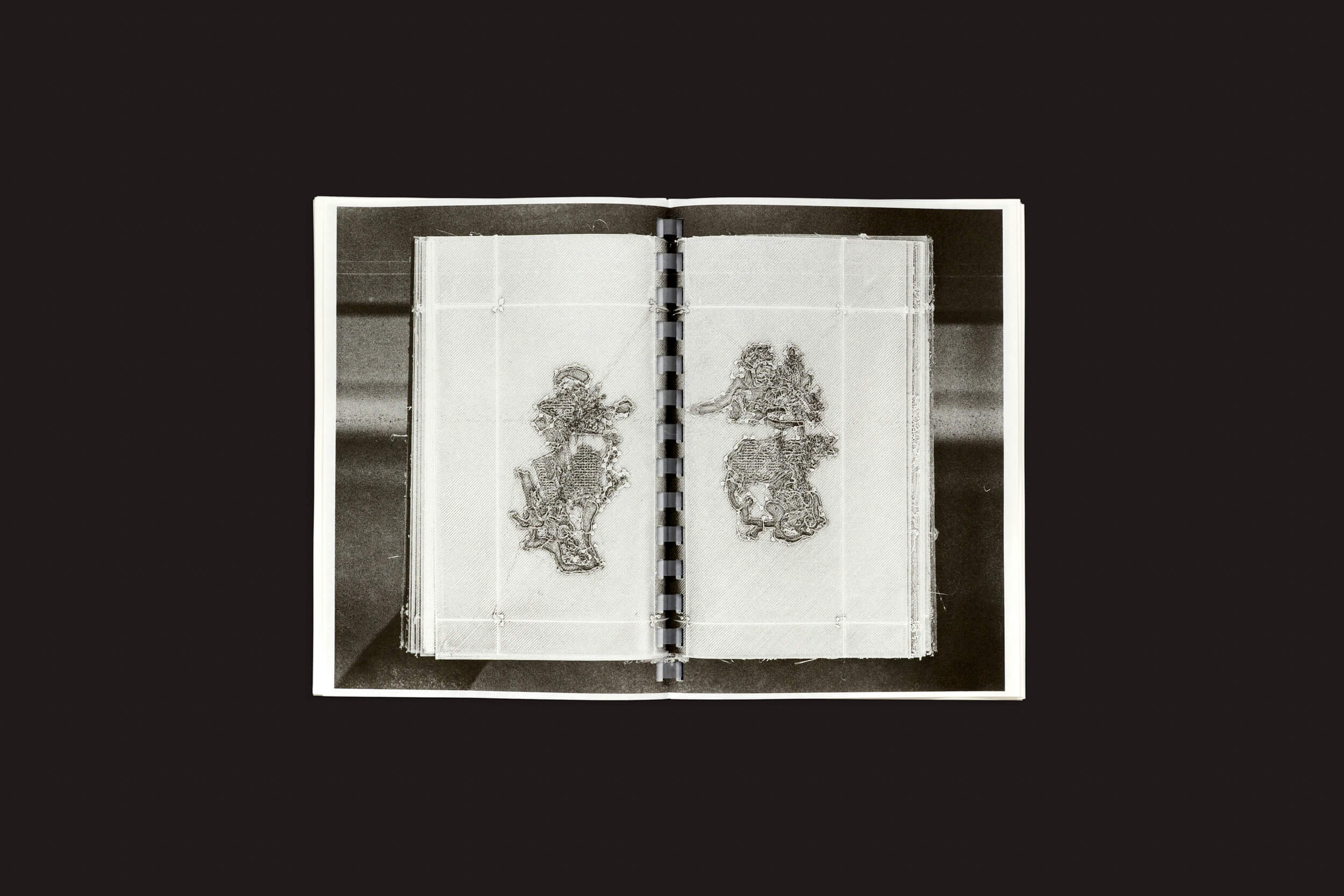 A imagem em tons de cinza de Darius Ou: Corpus da Temporary Press mostra um livro aberto, encadernado em espiral, com desenhos intrincados em forma de renda em um fundo simples e uma capa transparente, destacando a atenção excepcional aos detalhes do aclamado designer gráfico Darius Ou.