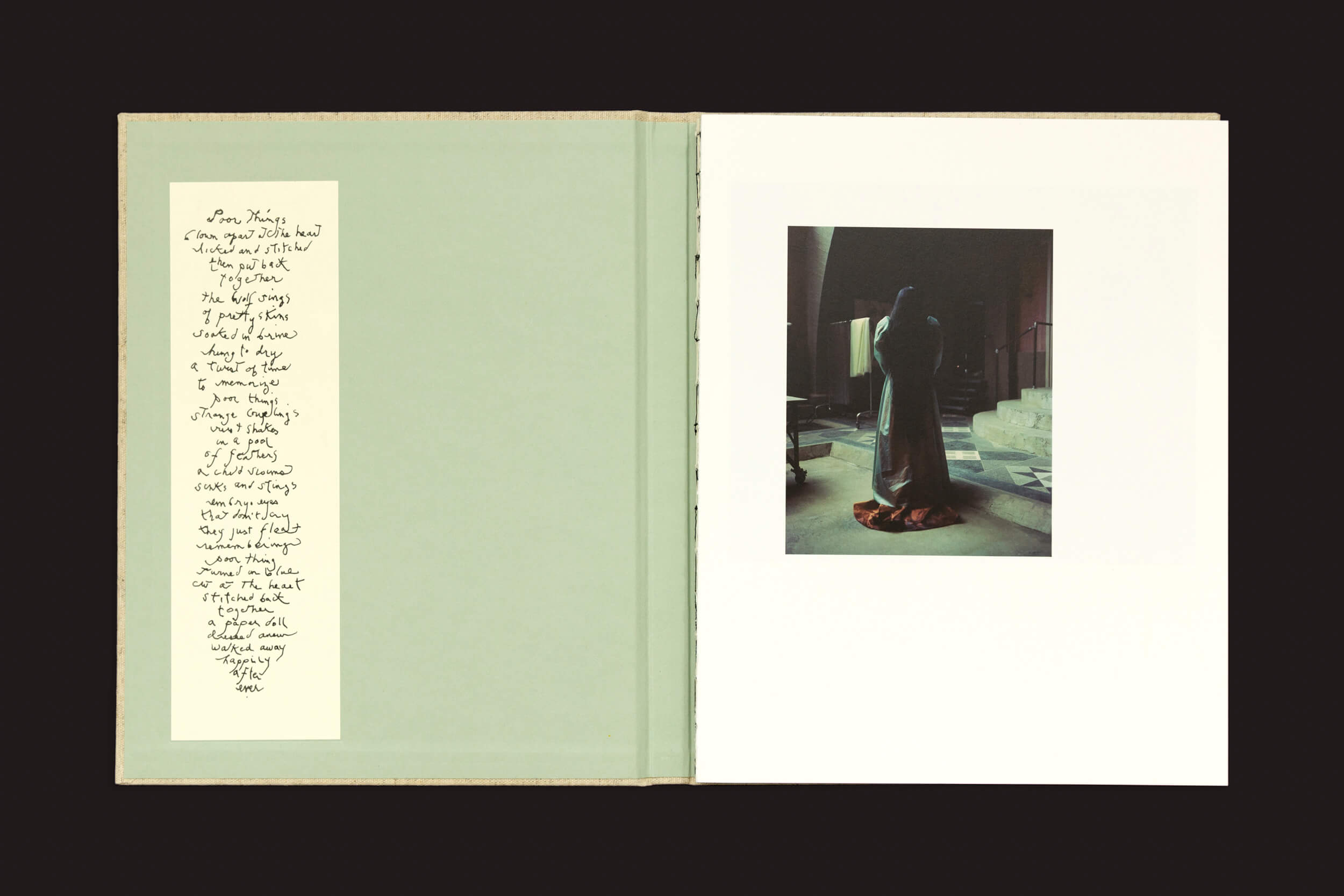 Um livro revela um poema escrito à mão à esquerda e uma foto impressionante de alguém nas escadas à direita. Em contraste com um verde suave, a cena reflete uma iluminação suave e dramática, semelhante ao estilo evocativo de Yorgos Lanthimos. Produto: Dear God, the Parthenon is still broken de Void.