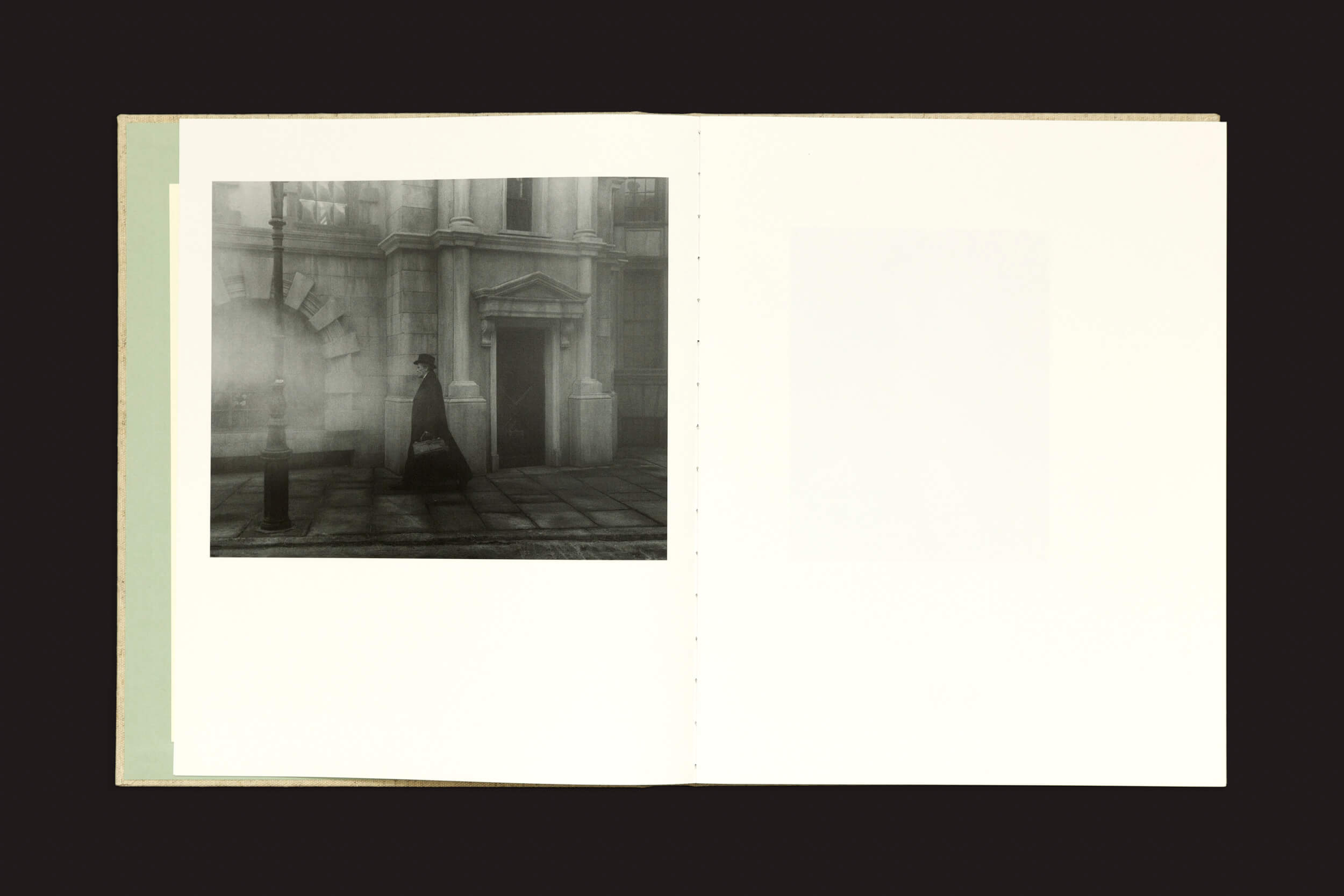 A página da esquerda apresenta uma foto em tom sépia de uma figura encapuzada perto de um edifício de pedra com uma entrada em arco, que lembra o estilo de Yorgos Lanthimos em Yorgos Lanthimos: Dear God, the Parthenon is still broken de Void. A página da direita está em branco em um fundo escuro, como um álbum de fotos do século XIX.