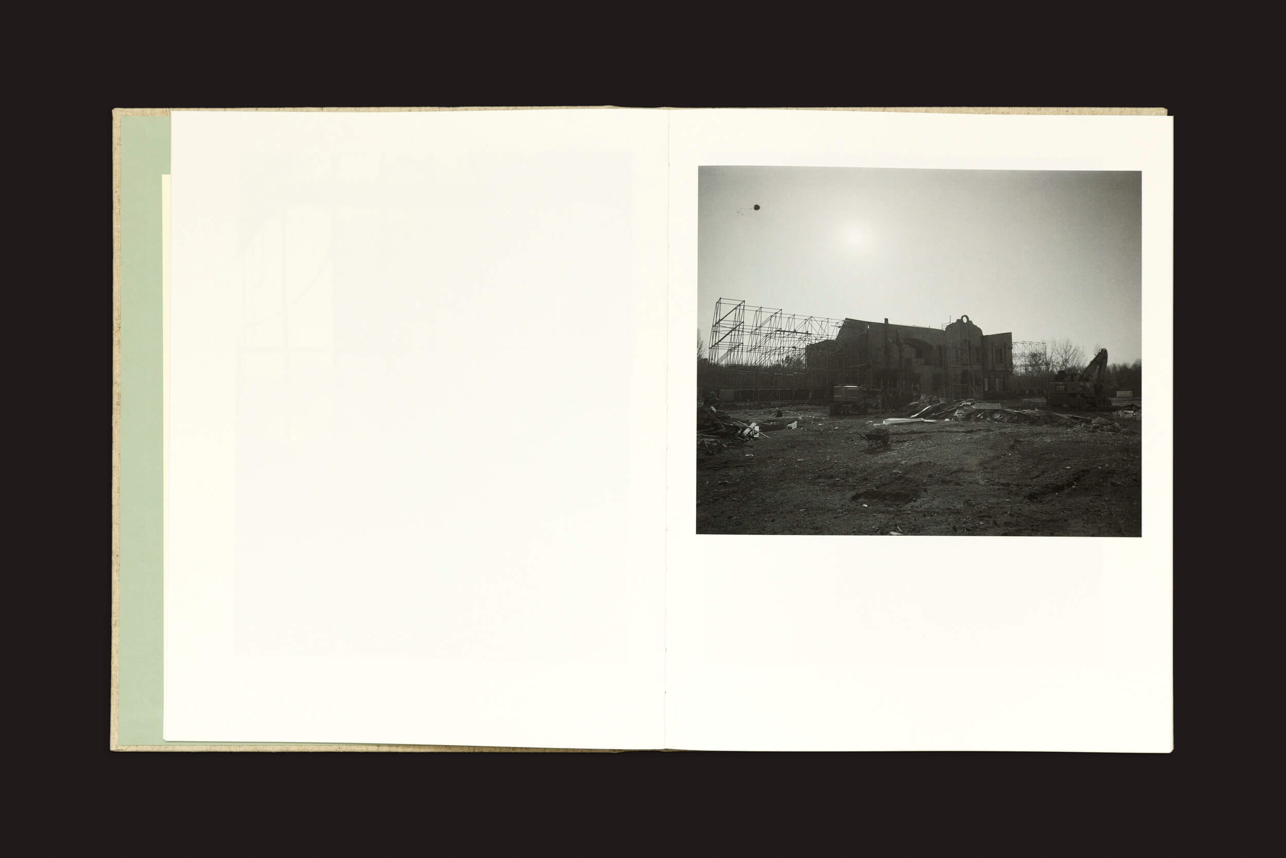 Páginas do livro Dear God, the Parthenon is still broken de Yorgos Lanthimos exibem uma foto em preto e branco na página direita de um prédio industrial com um telhado danificado sob céus brilhantes; a página esquerda apresenta contornos tênues que evocam o charme do século XIX. Marca: Void.