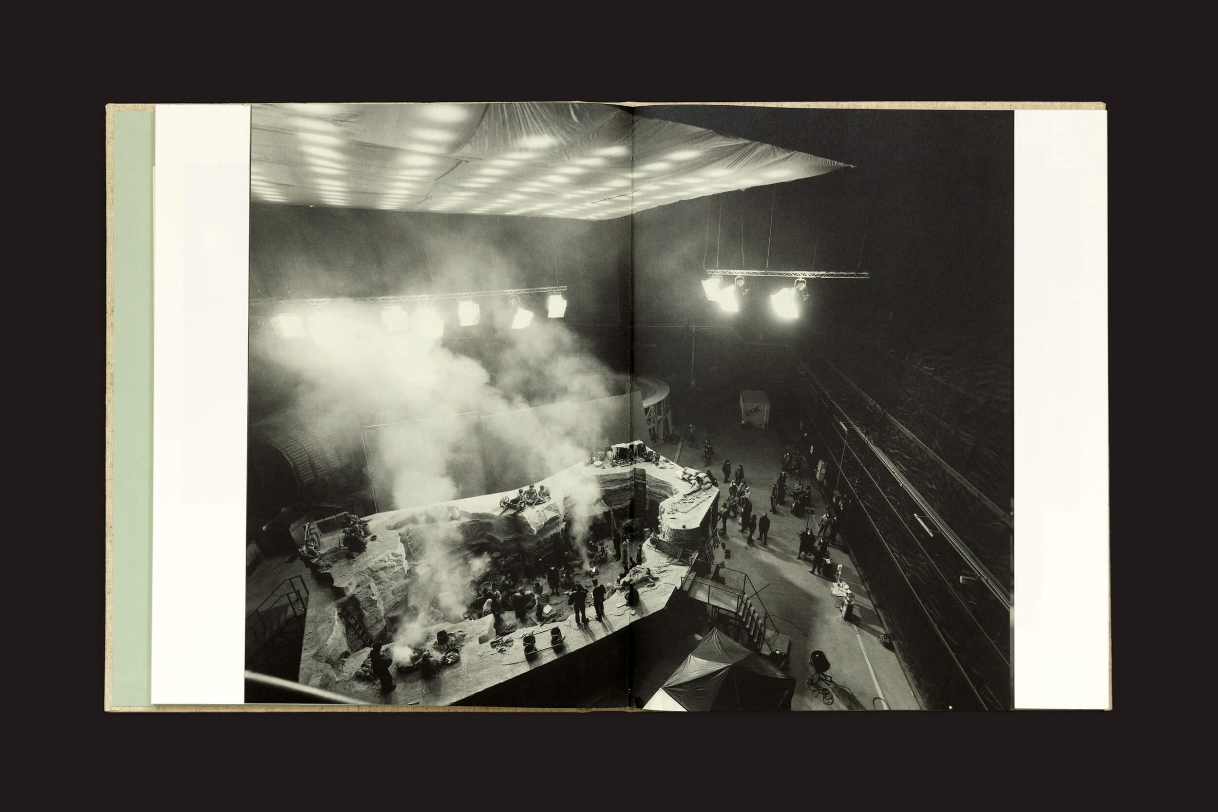 Uma foto em preto e branco de um set de filmagem de Yorgos Lanthimos: Dear God, the Parthenon is still broken da Void captura uma atmosfera cheia de fumaça, luzes brilhantes no teto e uma equipe agitada em torno de uma estrutura complexa que lembra as produções cinematográficas do século XIX.