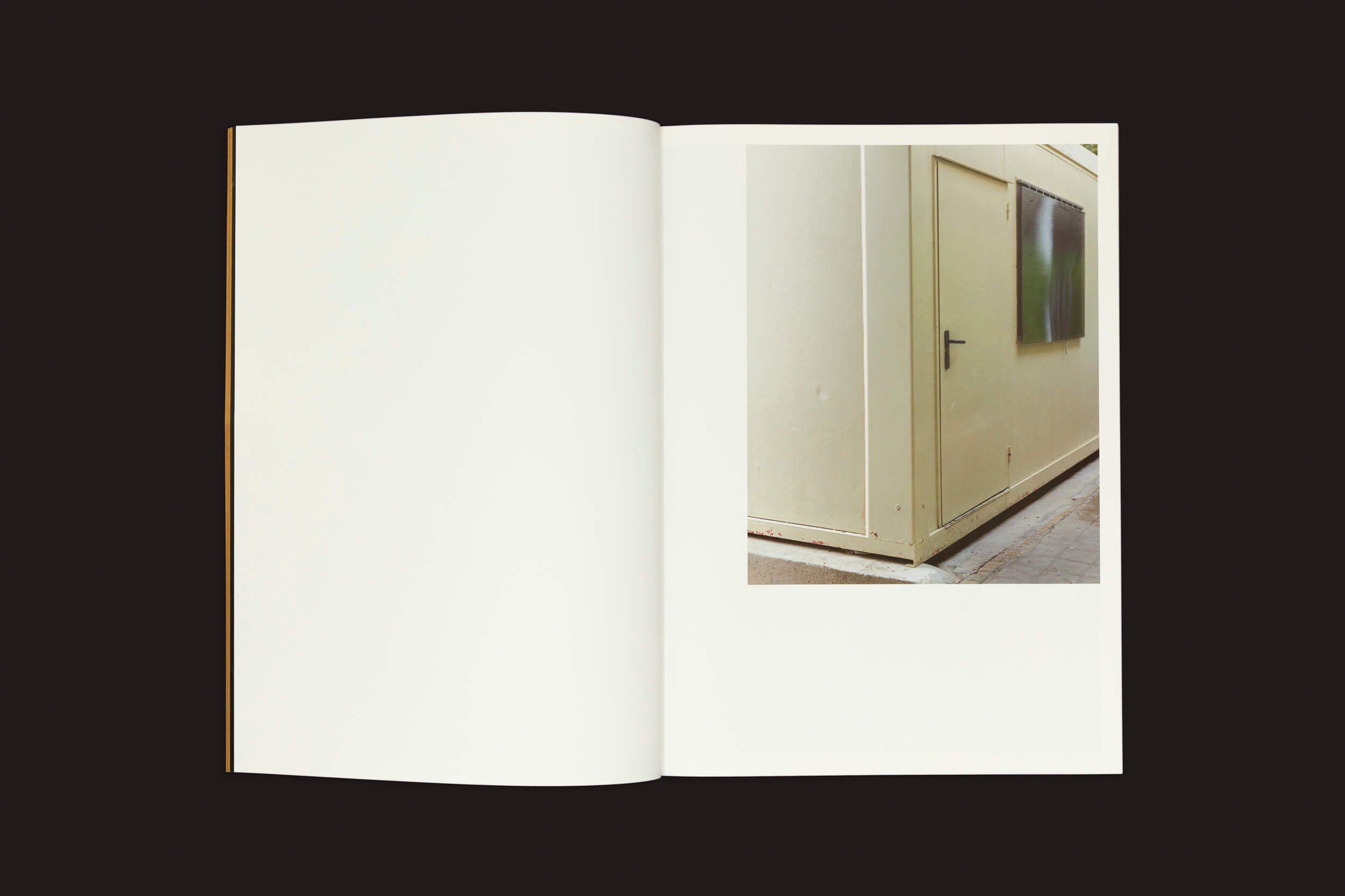 O livro Felipe Romero Beltrán: Dialect de Loose Joints é mostrado aberto em um fundo preto. A página da esquerda está em branco, enquanto a da direita retrata uma estrutura bege em forma de caixa com uma porta e janela, sugerindo os desafios enfrentados por imigrantes marroquinos lidando com status legal no exterior.