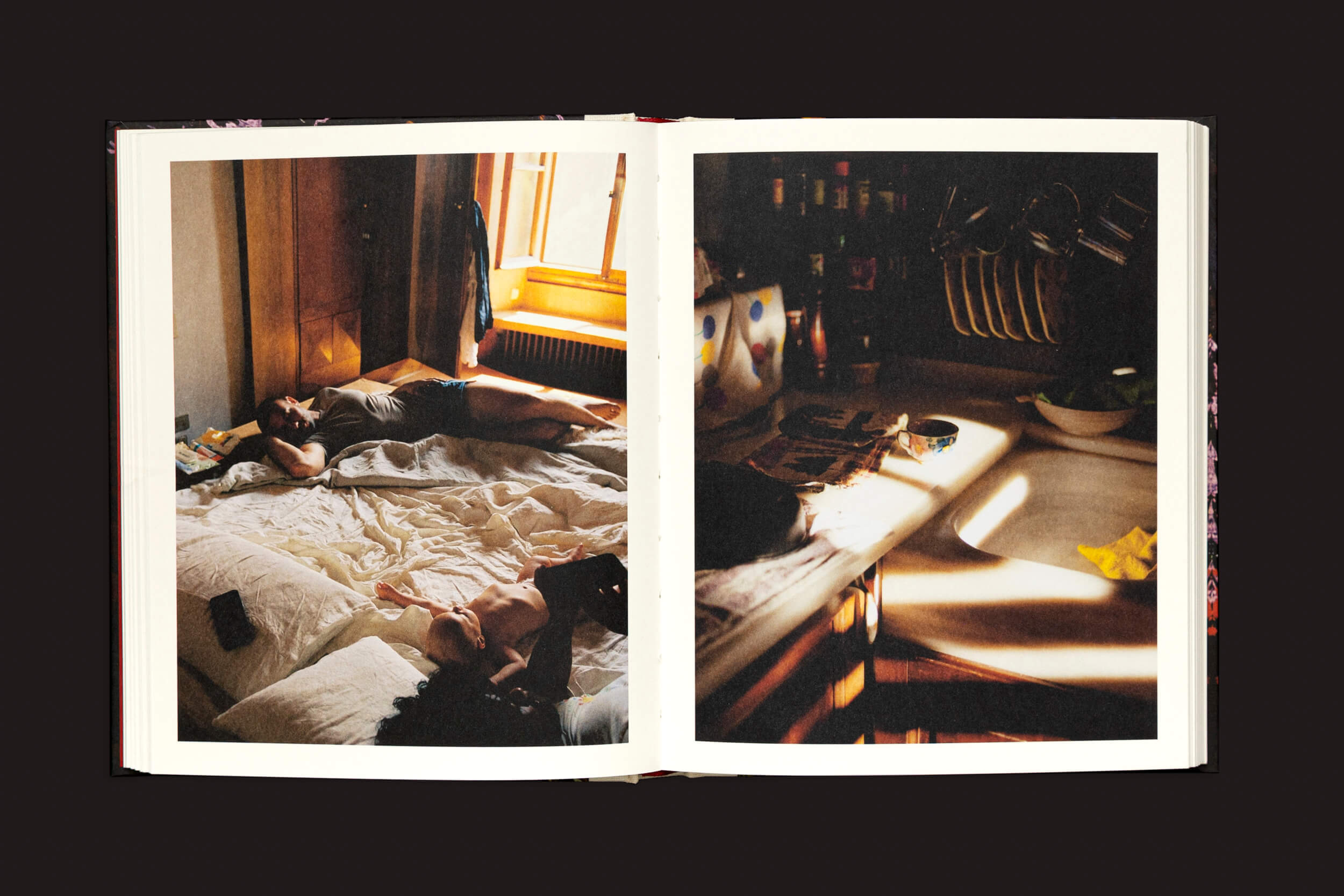 O livro Pia Riverola: Días de Loose Joints está aberto sobre uma superfície escura. Página da esquerda: duas pessoas em uma cama desfeita, mal iluminada com imagens evocativas de janelas. Página da direita: uma pia de cozinha desorganizada com pratos, utensílios e um pano amarelo oferece uma verdadeira experiência sensorial.