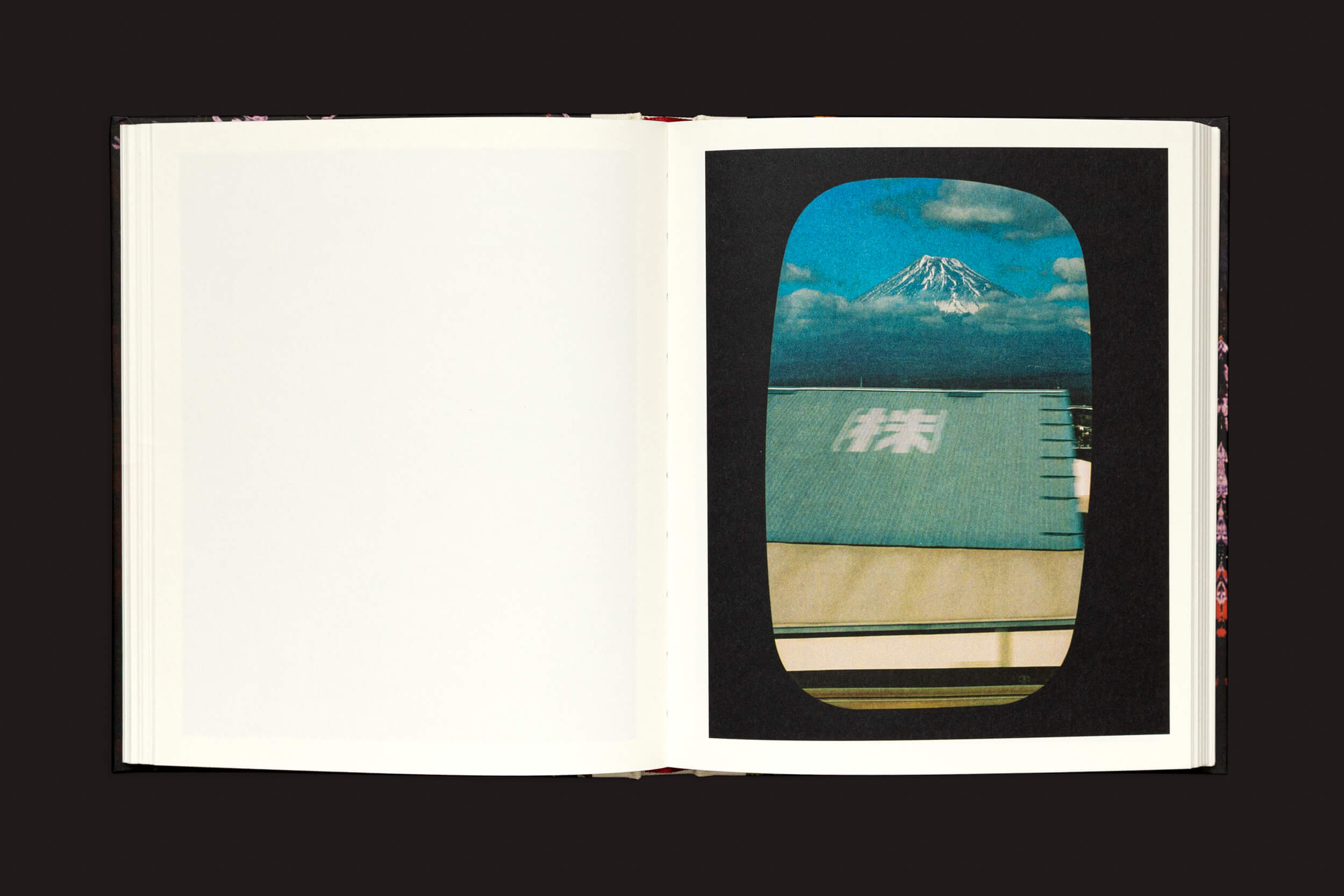 Em Pia Riverola: Días, de Loose Joints, o livro aberto sobre uma superfície escura exibe uma página esquerda em branco e uma página direita evocativa, com uma foto de uma montanha nevada sob um céu nublado, emoldurada por caracteres japoneses, semelhante à janela de um trem.