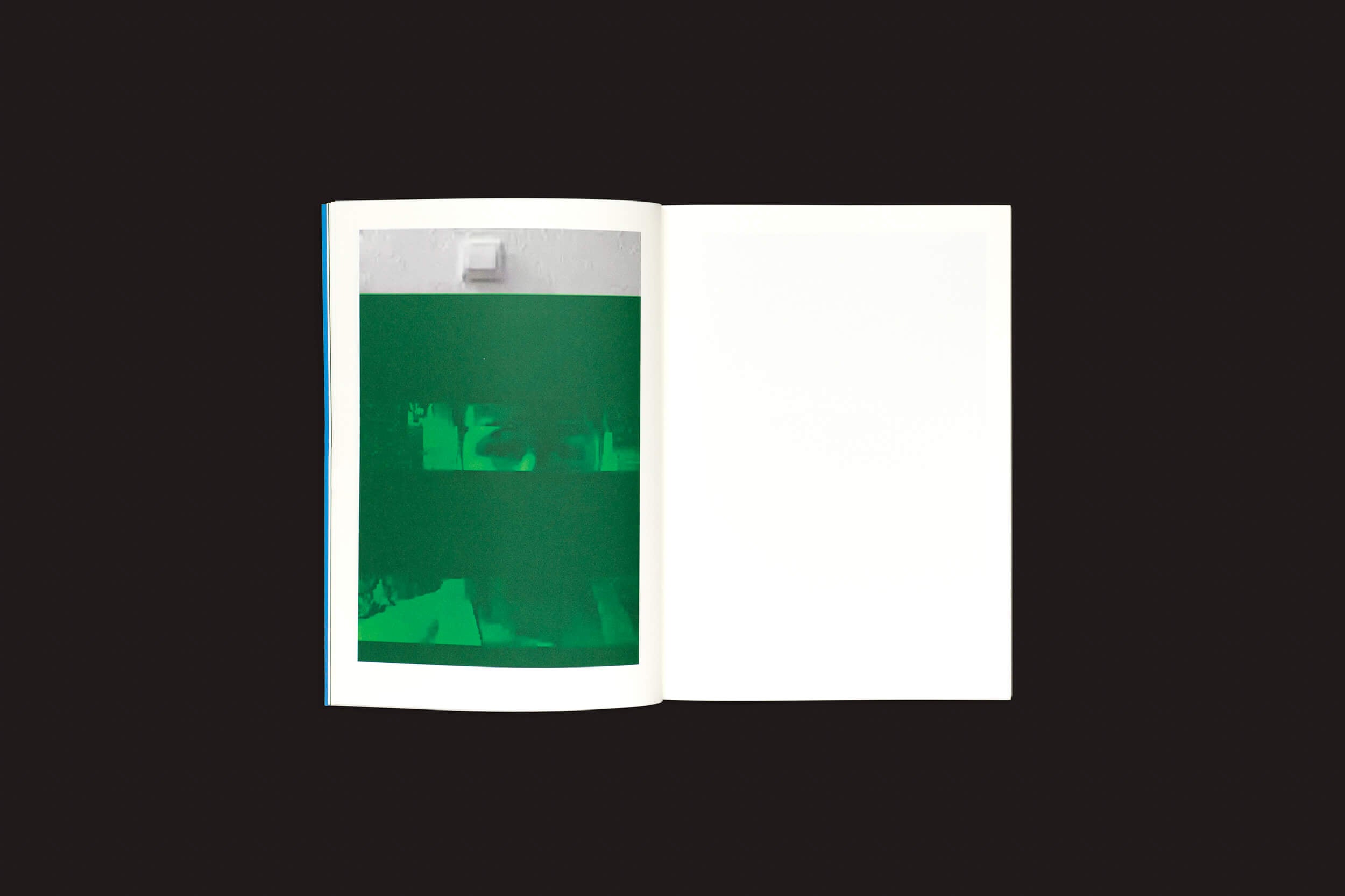 Um livro aberto, Taysir Batniji: Disruptions de Loose Joints, repousa sobre uma superfície escura. A página da esquerda apresenta uma imagem abstrata em tons de verde que lembra reflexões de Gaza, enquanto a página da direita está em branco, convidando à contemplação em meio a interrupções.