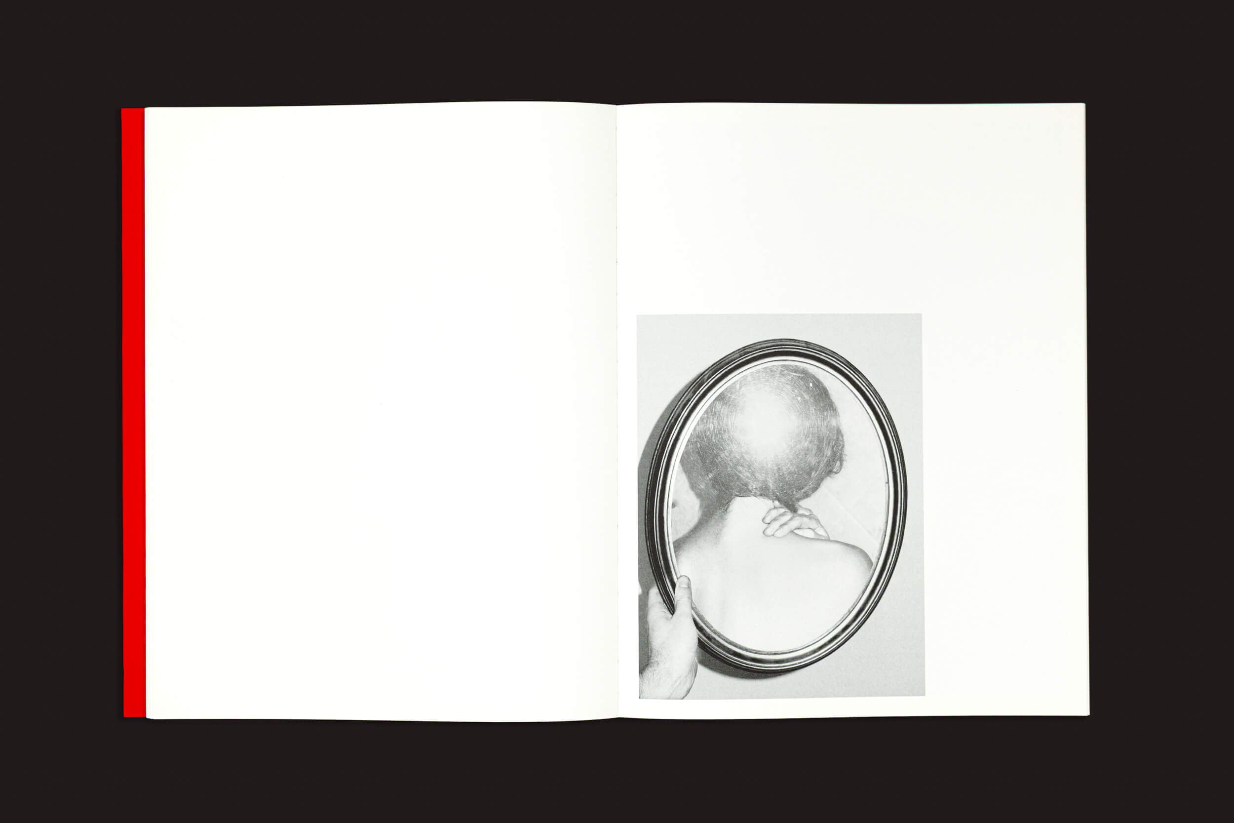 Um livro aberto, "Yurian Quintanas Nobel: Dream Moons", da editora Void, repousa sobre uma superfície escura, exibindo uma foto em preto e branco de alguém segurando um espelho redondo que reflete a parte de trás da cabeça. A lombada vermelha adiciona um ar de sonho bizarro à cena, já que a página da esquerda permanece em branco.