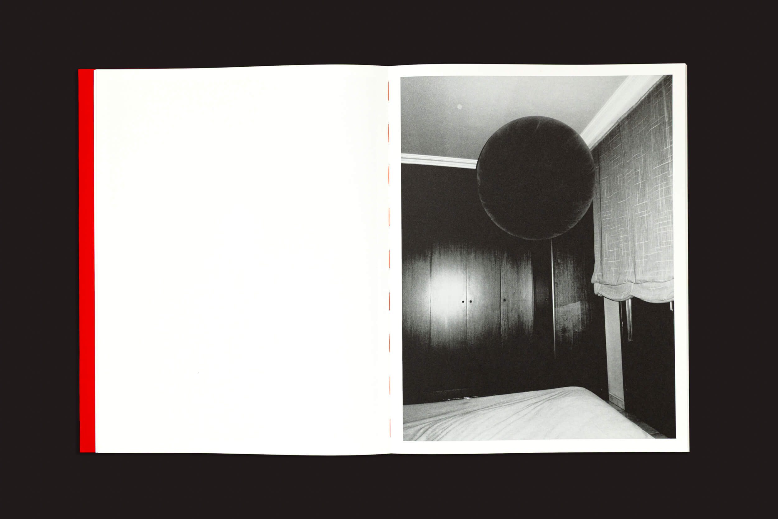 A imagem de um livro aberto sobre fundo preto apresenta "Luas de Sonho", de Yurian Quintanas, Nobel de Vazio. A página da esquerda está em branco, com uma borda vermelha, contrastando com a da direita, que mostra sua fotografia de um quarto com um objeto grande e redondo flutuando assustadoramente perto do teto — um verdadeiro sonho bizarro.