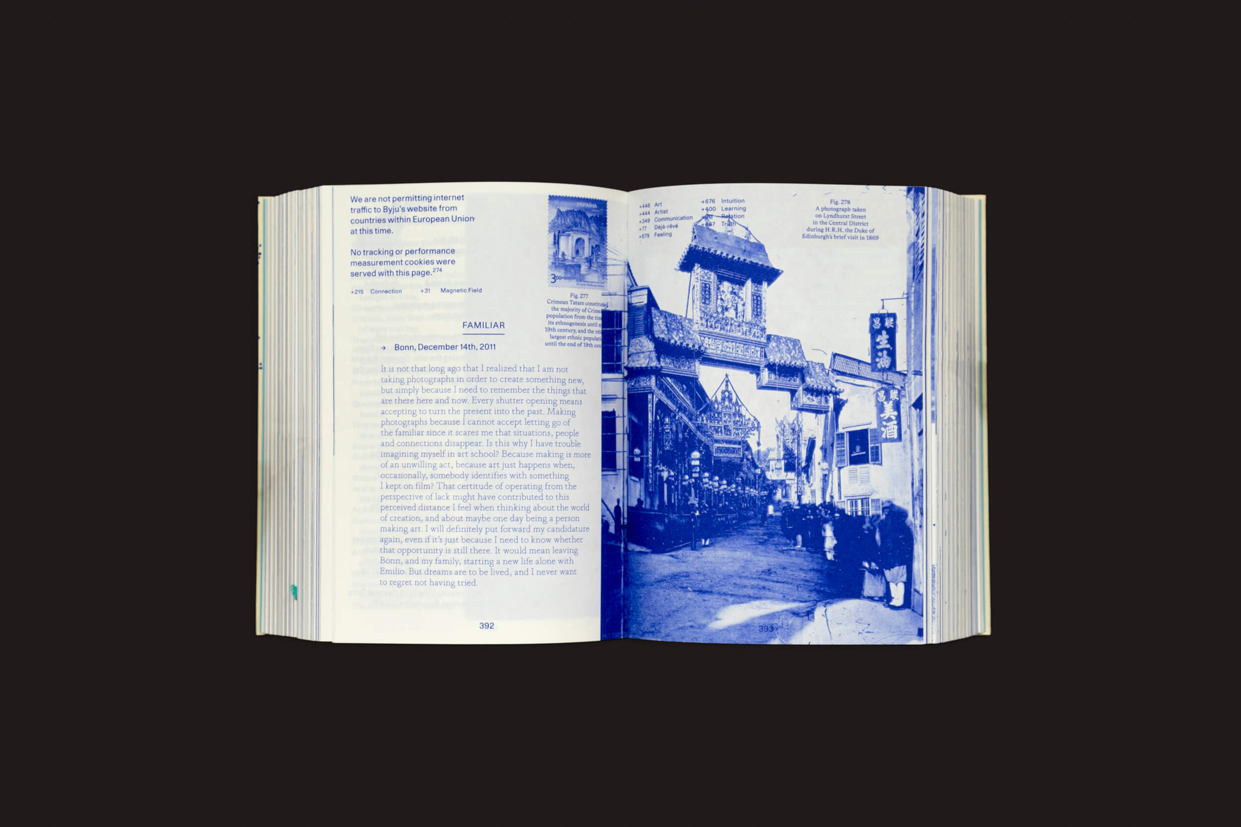 Um livro aberto revela Anna Püschel: Encyclopedia of the Uncertain, de The Eriskay Connection, à esquerda, em frente a uma foto em tons de azul de uma rua oriental com telhados ornamentados e pedestres, evocando uma sensação de incerteza em meio à vida agitada.
