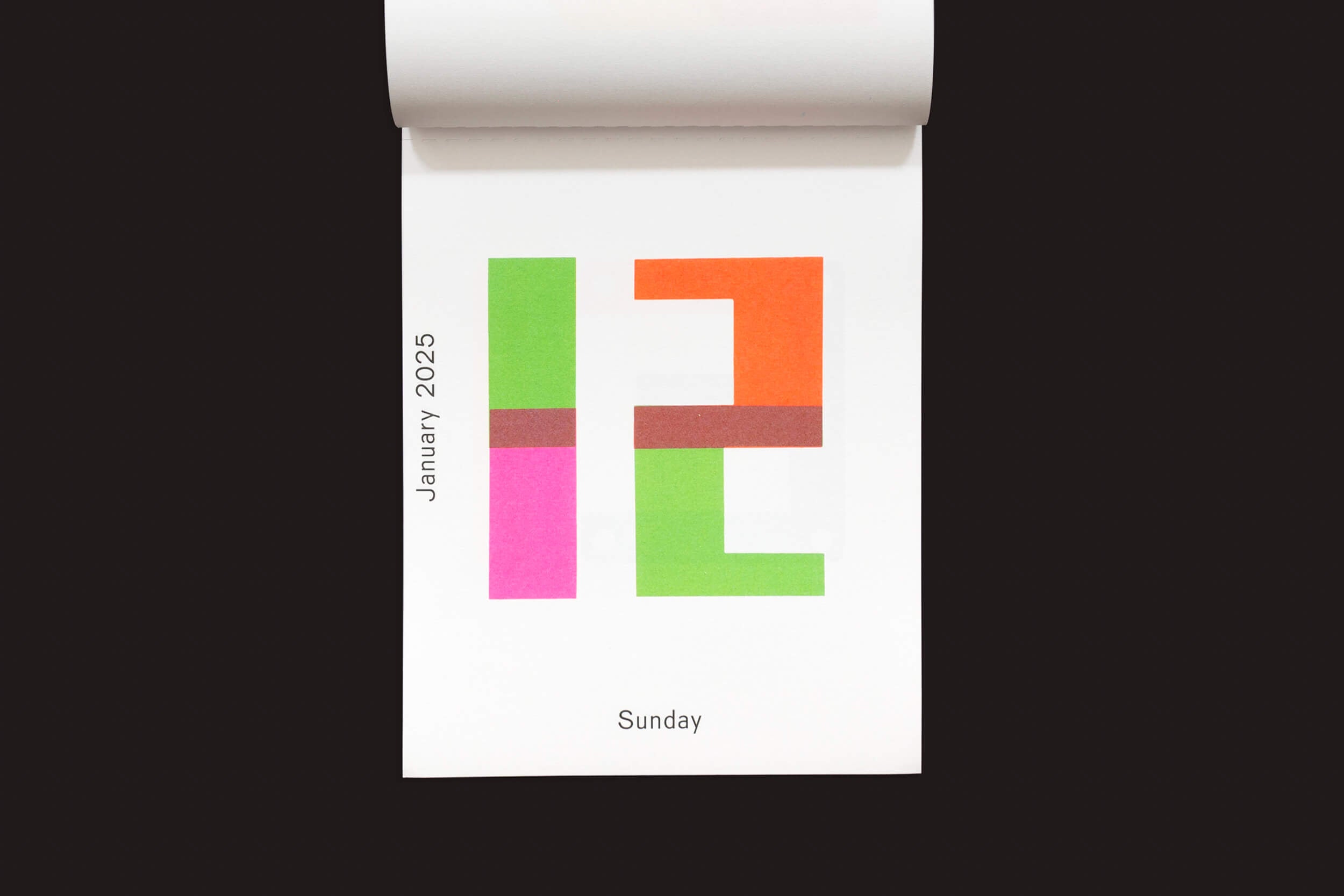 Uma página da Roma Publications Karel Martens: Calendário 2025 / Cada dia é um novo dia para domingo, 12 de janeiro, apresenta um design ousado da Karel Martens com o número 12 em blocos vibrantes de verde, rosa, vermelho e laranja sobre um fundo branco que lembra impressões tipográficas mono.