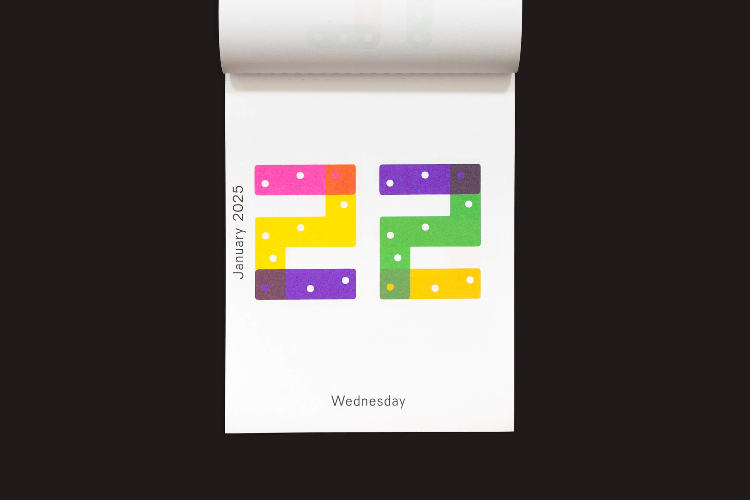 O Karel Martens: Calendar 2025 / Every day is a new day da Roma Publications apresenta Janeiro de 2025 à esquerda com 22 em blocos gradientes coloridos e em negrito que lembram o estilo de Karel Martens, e Quarta-feira na parte inferior sobre um fundo preto.