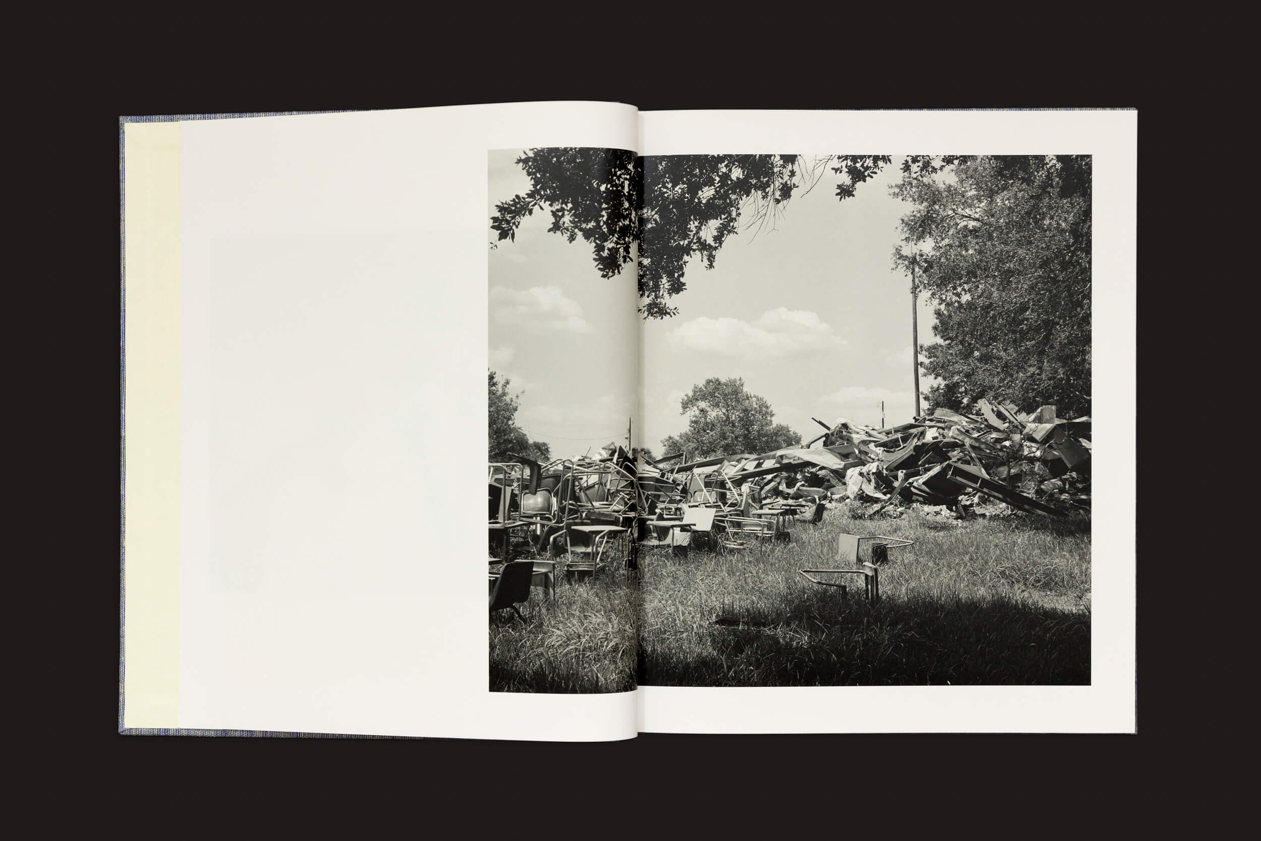 Um livro aberto de Rahim Fortune: Hardtack da Loose Joints revela uma foto em preto e branco de um ferro-velho com restos de metal espalhados sob um céu parcialmente nublado. As árvores na imagem ecoam sutilmente a mistura de progresso industrial e beleza natural da América pós-emancipação.