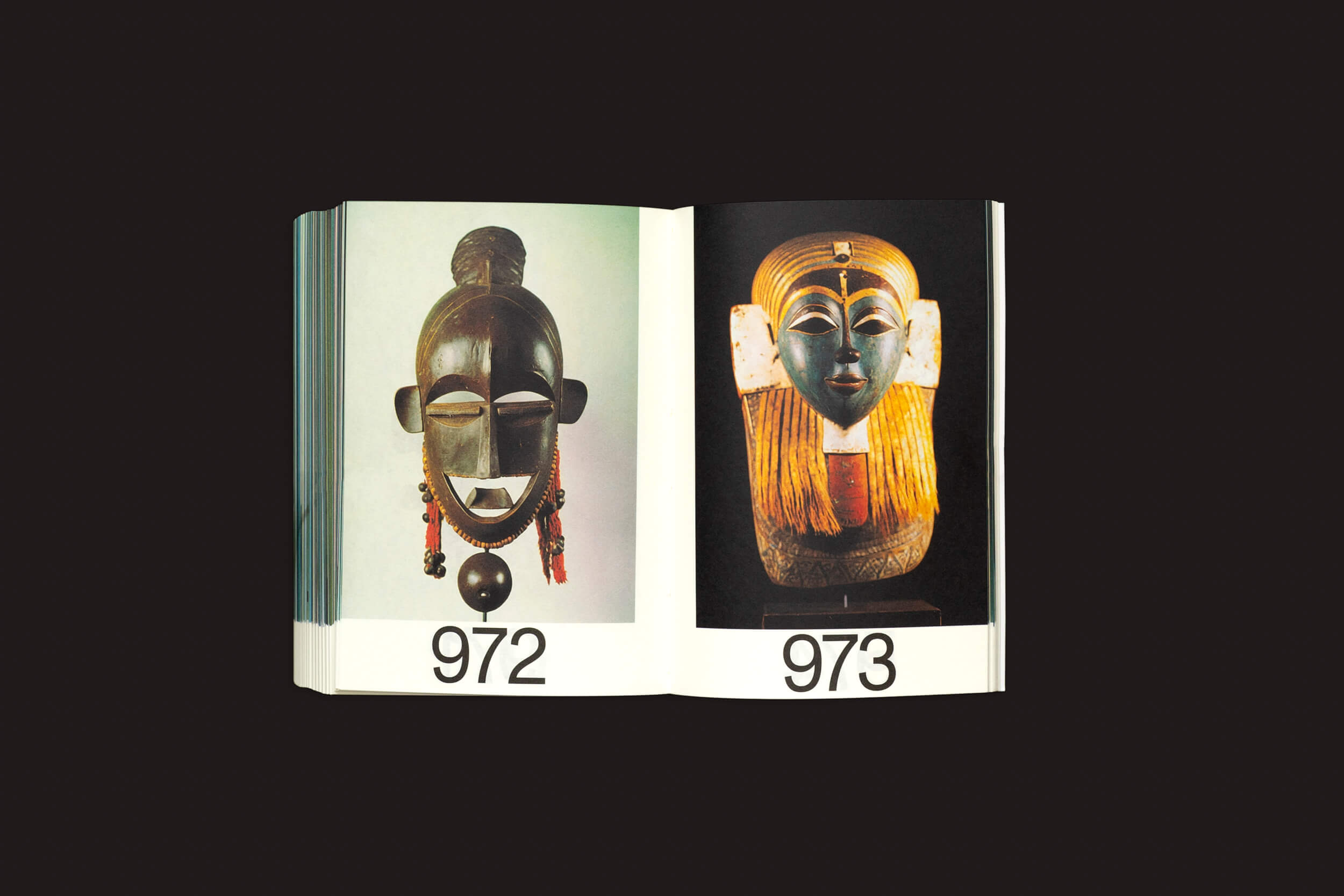 O livro aberto Martín Bollati: Hermes/Unesco da SED Editorial revela as páginas 972 (uma máscara de madeira escura com olhos grandes, evocando civilizações antigas) e 973 (uma máscara colorida adornada com detalhes em dourado e vermelho, que lembra tesouros arqueológicos).