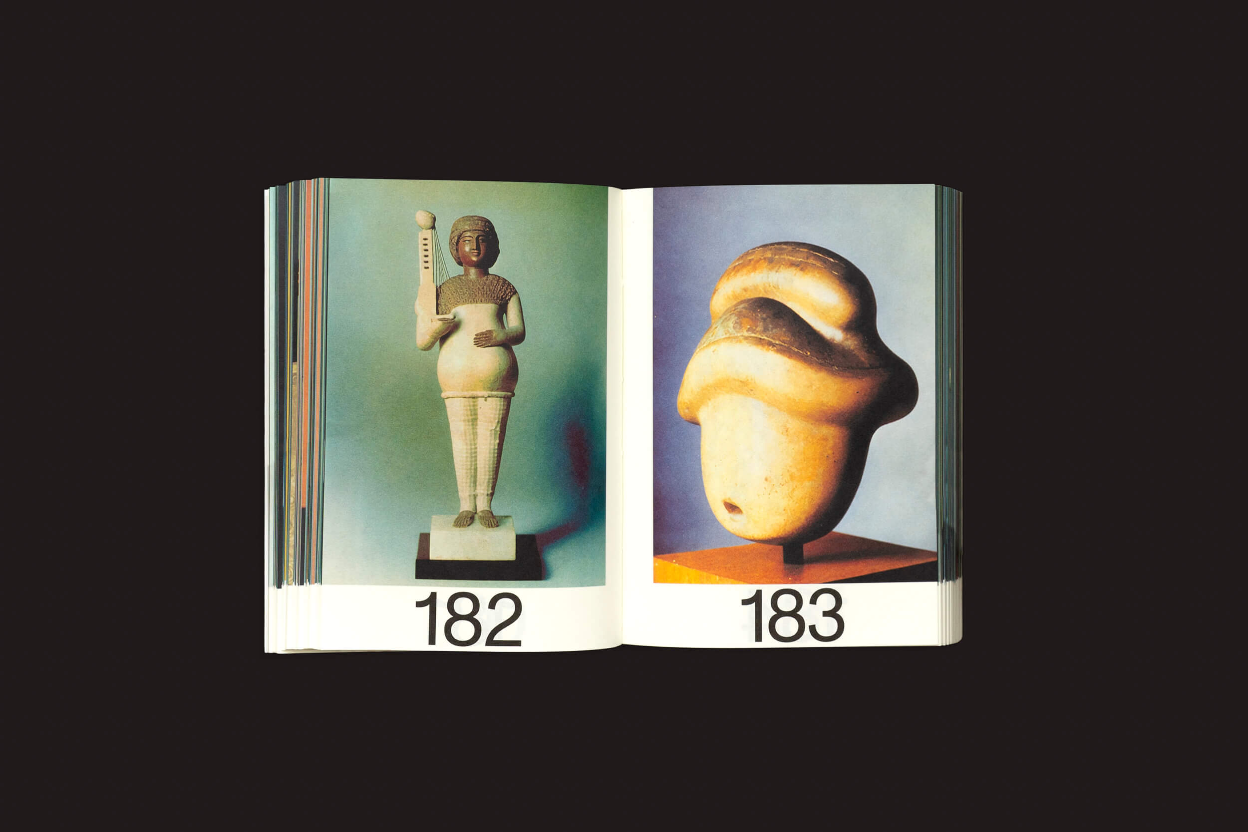 O livro Martín Bollati: Hermes/Unesco da SED Editorial abre revelando uma estátua humanoide abstrata com um cajado na página esquerda, numerada 182, e uma cabeça antiga na direita, numerada 183. O fundo preto realça essas obras de arte arqueológicas de civilizações antigas.