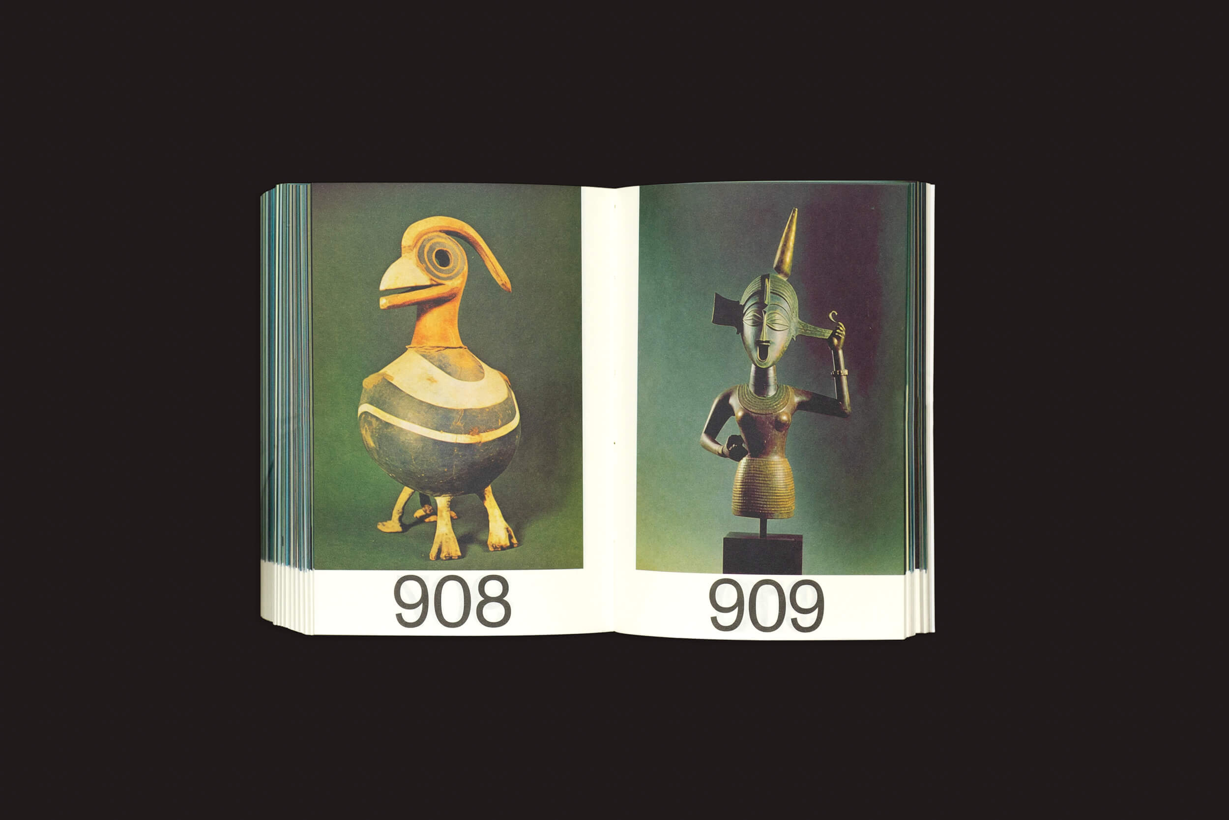 Um livro aberto revela duas páginas: a da esquerda apresenta um artefato em forma de pássaro rotulado como 908, evocando civilizações antigas; a da direita mostra uma estátua semelhante a um humano numerada como 909. O fundo escuro acrescenta mistério a esses tesouros em Martín Bollati: Hermes/Unesco da SED Editorial.