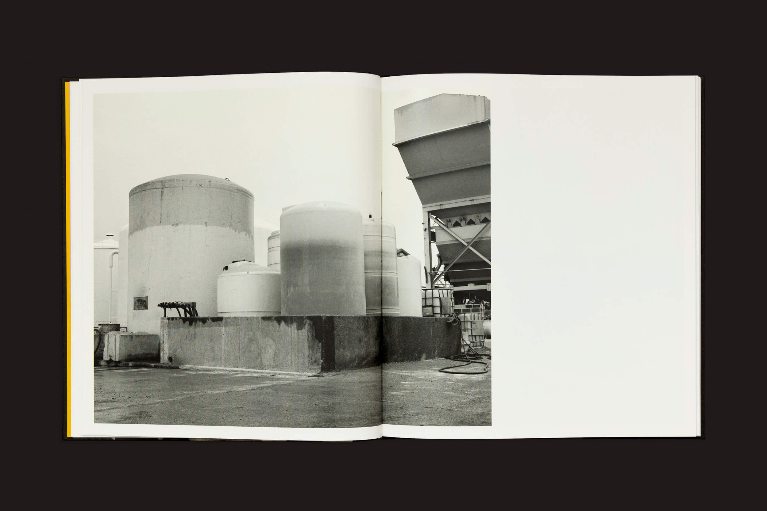 Um livro aberto, Rahim Fortune: I Cant Stand to See You Cry, de Loose Joints, revela uma foto em preto e branco da indústria do Texas. Grandes tanques cilíndricos e armações de metal contrastam com um fundo simples, destacando a beleza austera da imagem com texto mínimo.