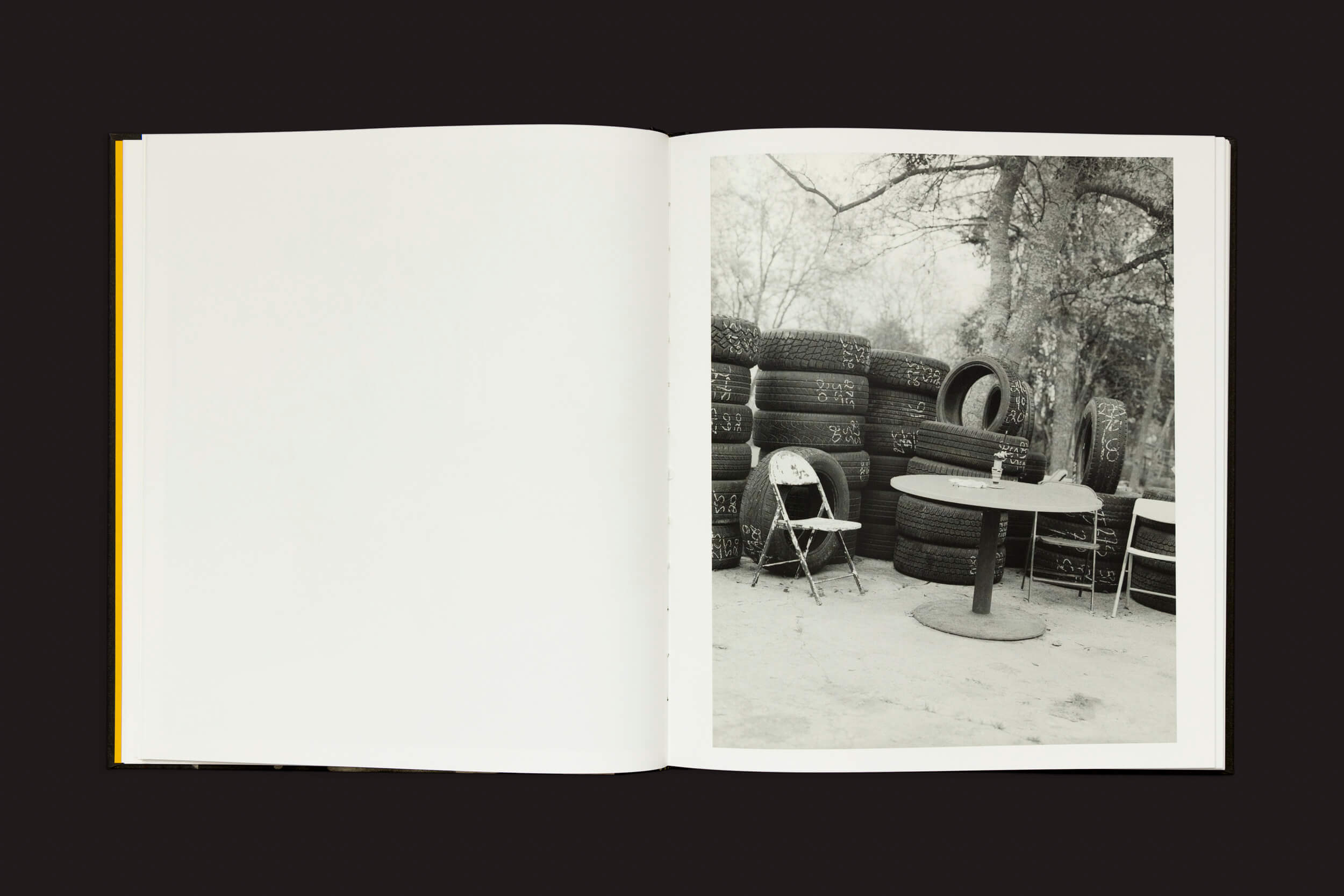 Uma página de Rahim Fortune: I cant stand to see you cry de Loose Joints apresenta uma foto monocromática de pneus ao lado de uma cadeira dobrável e uma mesa redonda, capturando a sensação rústica do Texas. Árvores nuas podem ser vistas ao fundo, com a página esquerda em branco.