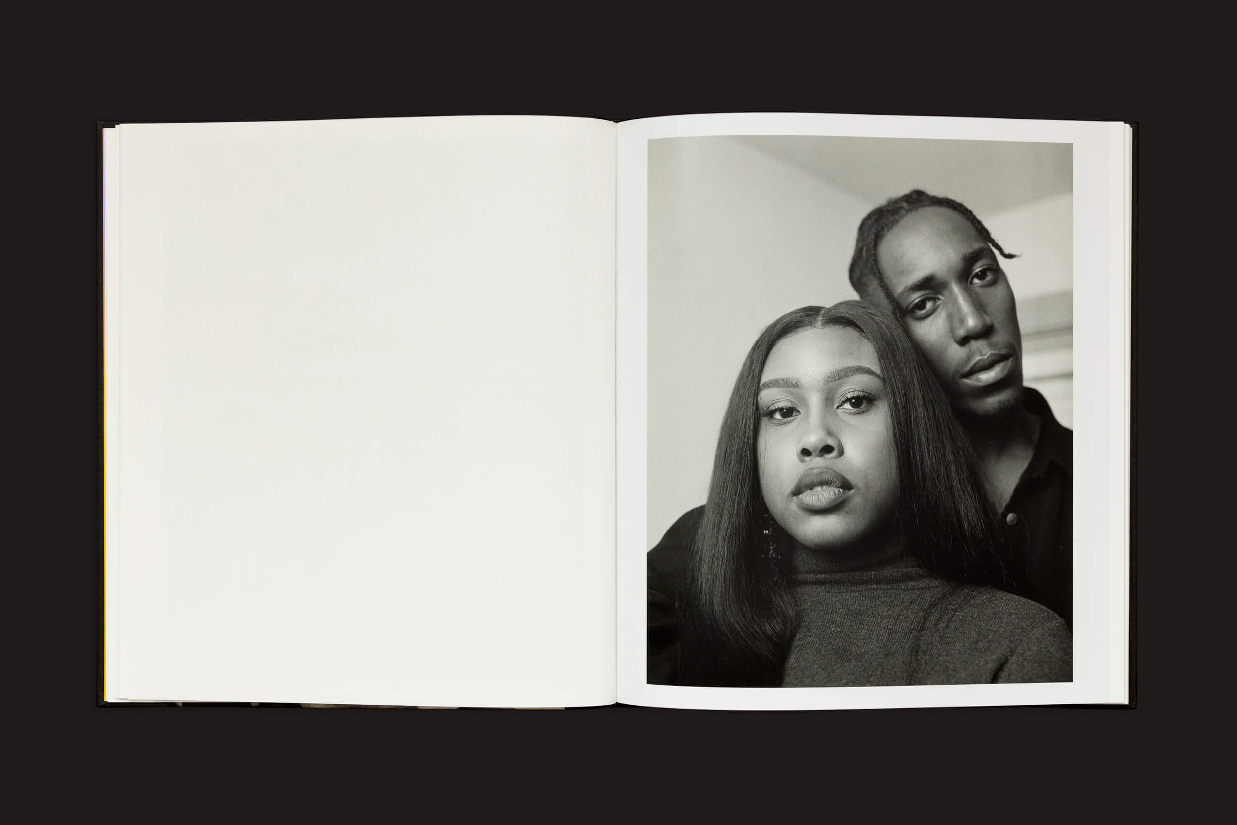 Uma cópia de Rahim Fortune: I cant stand to see you cry de Loose Joints está aberta sobre uma superfície escura, mostrando uma foto em preto e branco de duas pessoas explorando suas identidades: uma com cabelo longo em primeiro plano, e outra com cabelo trançado ligeiramente atrás. A página oposta está em branco.