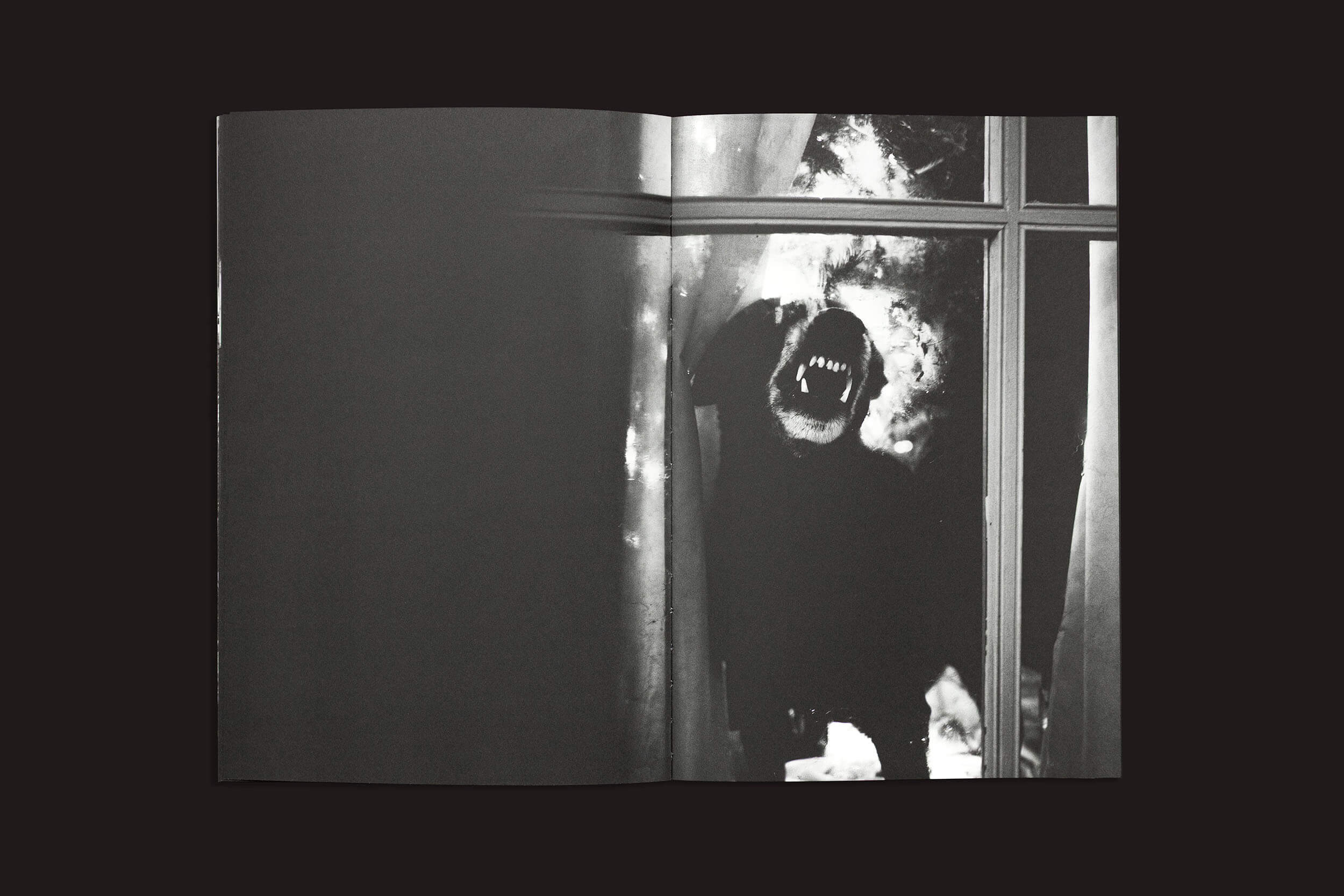 Em uma imagem em preto e branco de "Gui Marcondes: Eu sei que existo porque você me imagina", da Nearest Truth Editions, uma figura escura com um rosto assustador espia através de uma janela, incorporando a exploração de Gui Marcondes da experiência humana da incerteza contra cortinas mal iluminadas.