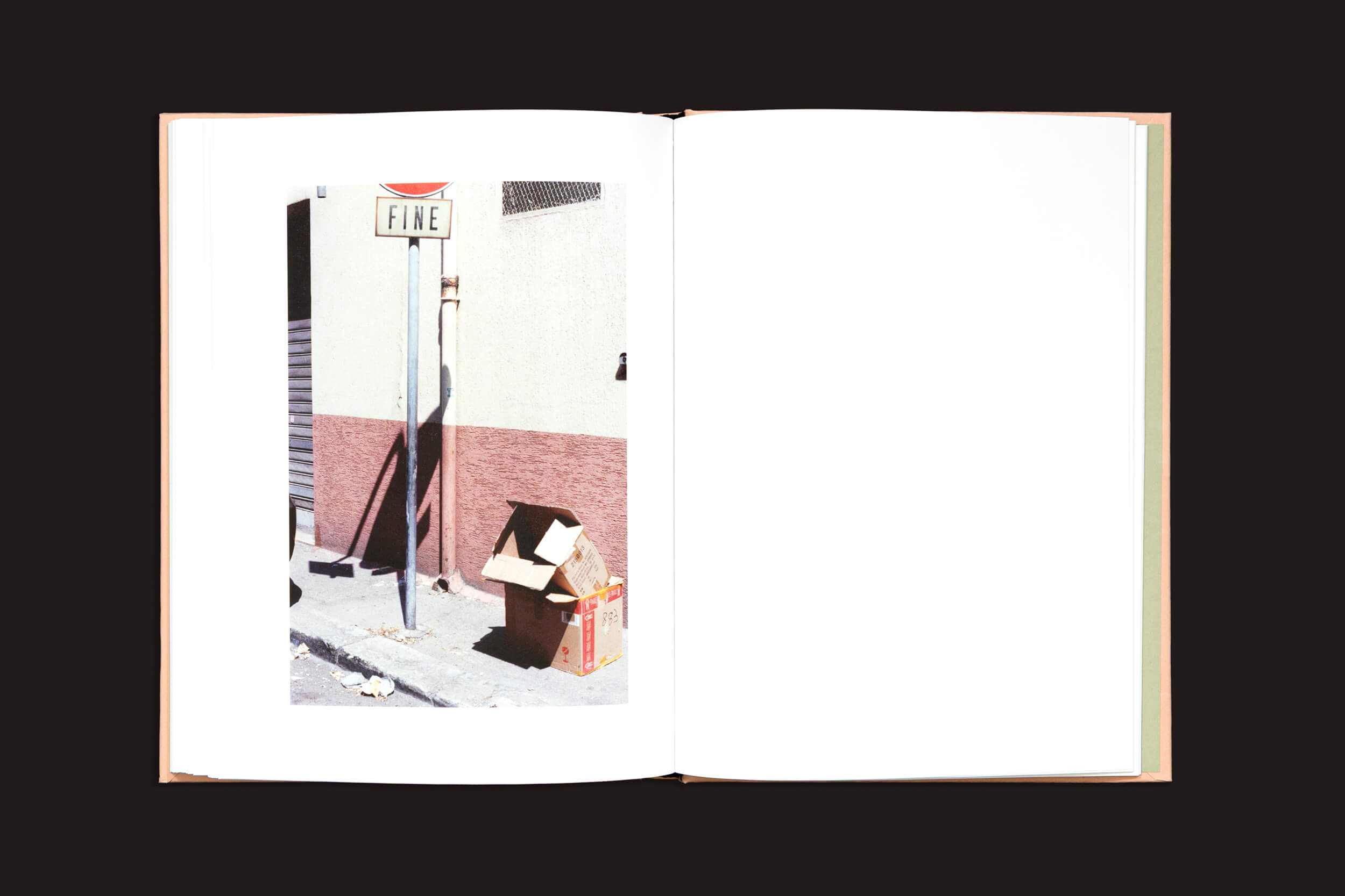 Um livro fotográfico aberto, "Federico Clavarino: Italia O Italia", de Void, exibe uma cena de rua na página da esquerda, com uma placa de FINE em um poste e caixas de papelão vazias encostadas em um prédio. A página da direita permanece em branco, convidando à contemplação.