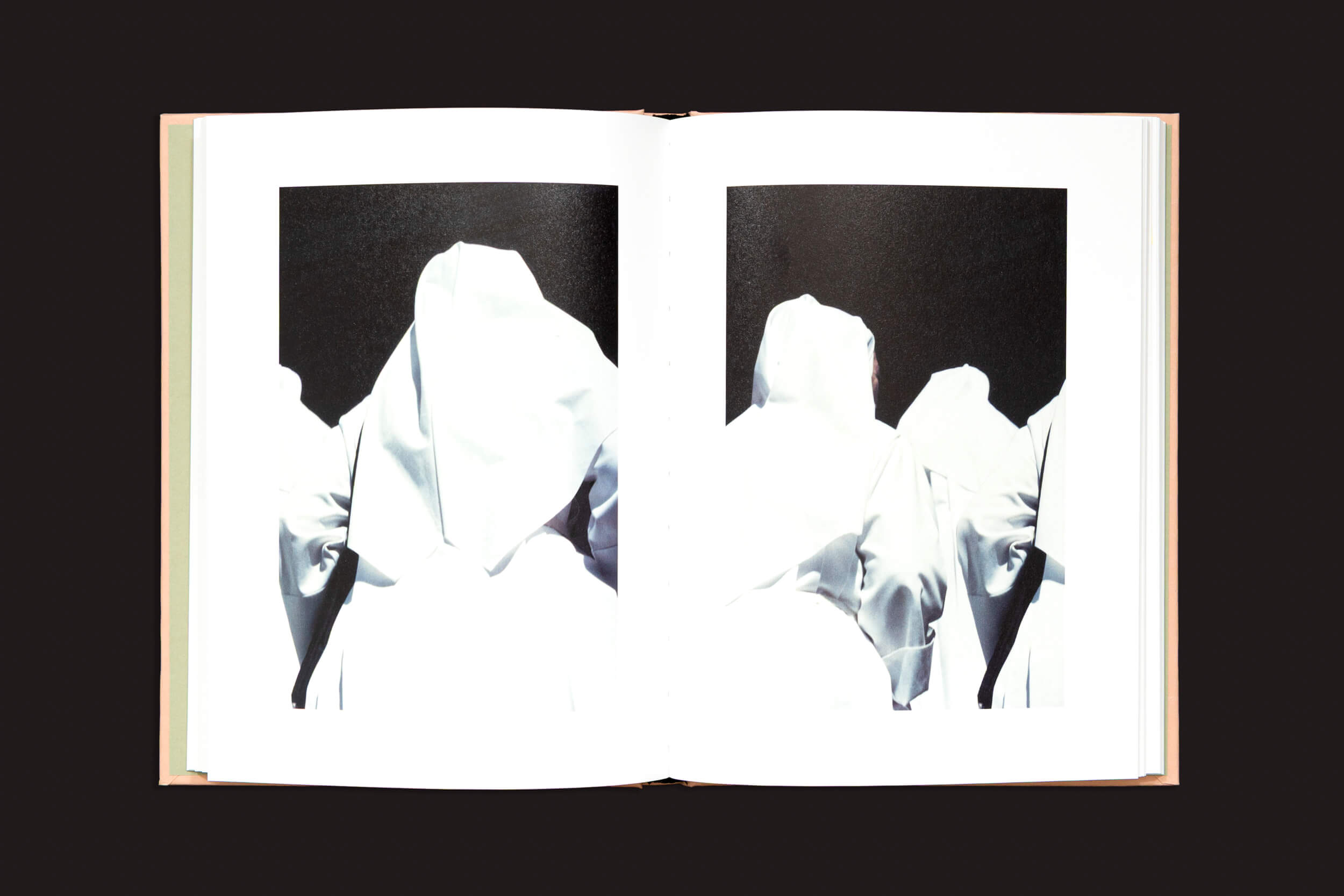 Em "Italia O Italia", de Federico Clavarino, da Void, um livro aberto hipnotizante revela uma fotografia simbólica com figuras em trajes brancos com capuz sobre um fundo escuro, criando um contraste impressionante em seu estilo distinto.