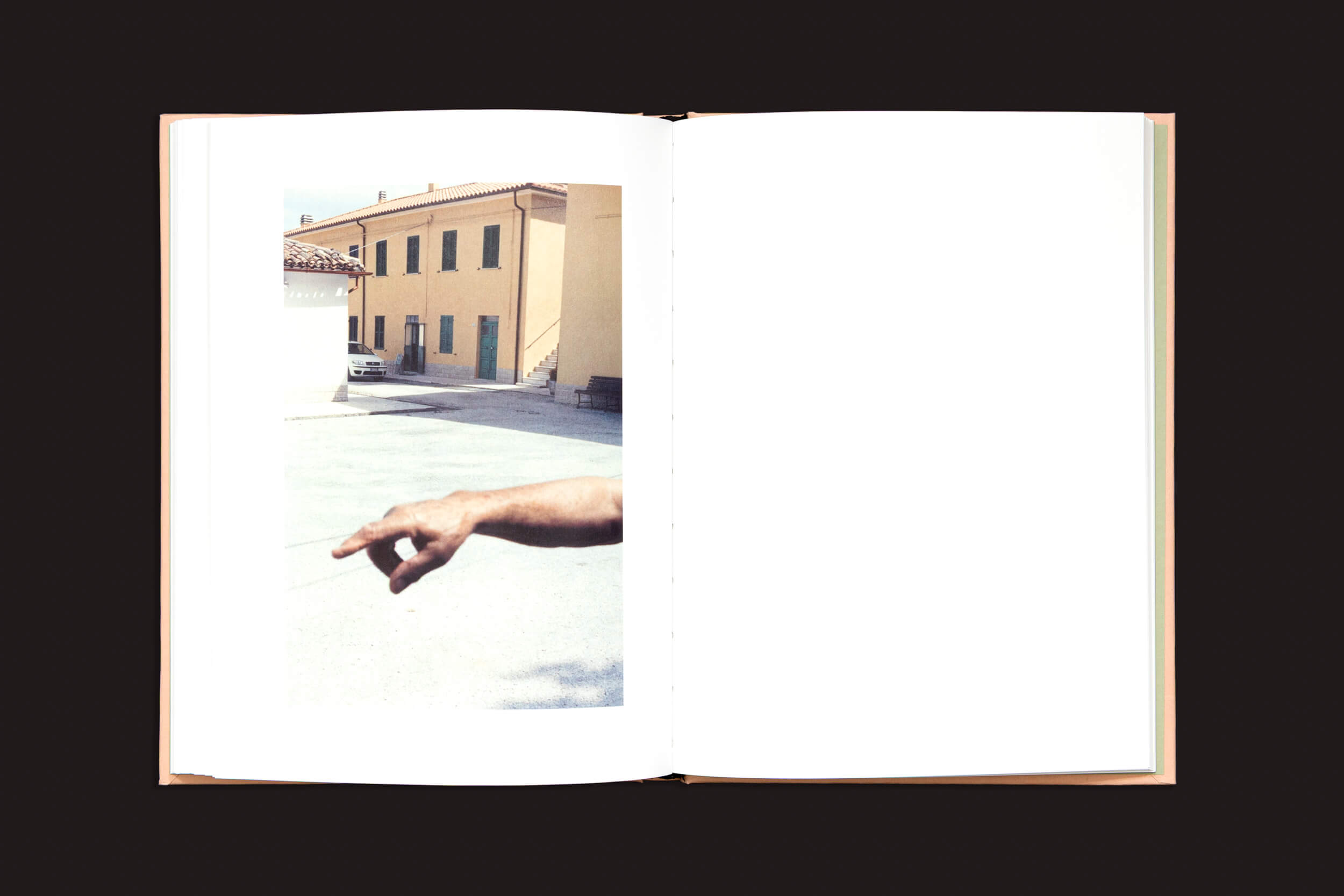 Um livro aberto intitulado "Federico Clavarino: Italia O Italia", da Void, mostra a foto de um prédio bege de dois andares com persianas verdes. Um braço aponta para o prédio em primeiro plano, exibindo o estilo de Federico Clavarino contra um fundo preto sólido.