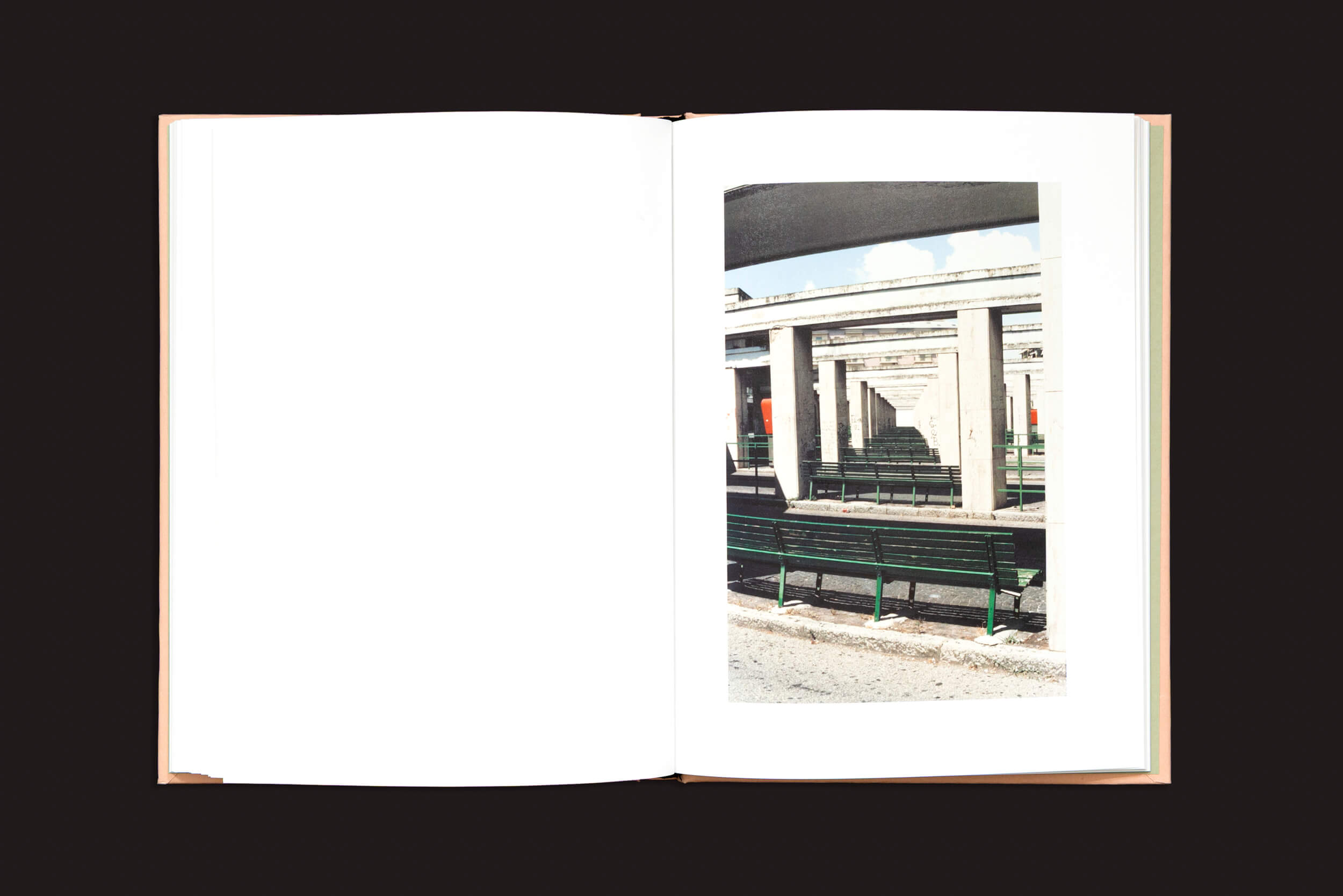 O livro aberto "Federico Clavarino: Italia O Italia", de Void, está sobre um fundo preto simples, exibindo uma foto de uma estrutura arquitetônica com colunas e bancos na página direita, enquanto a página esquerda permanece em branco.