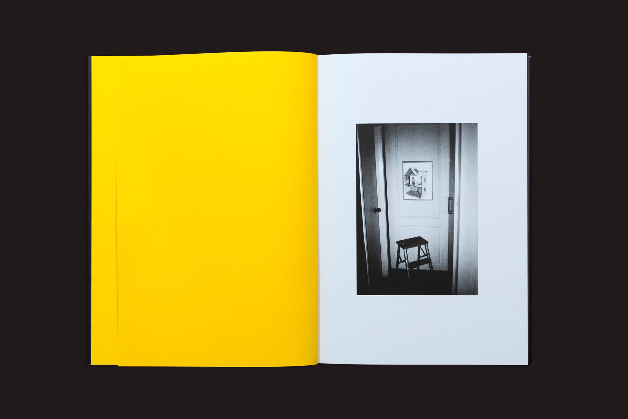 Um livro do Selo Turvo apresenta uma página esquerda amarela brilhante e uma página direita branca, exibindo uma fotografia em preto e branco de Artur Lahoz. Ela retrata um simples banco de madeira diante de uma porta fechada com uma moldura, evocando a essência do Klexos contra o fundo escuro.