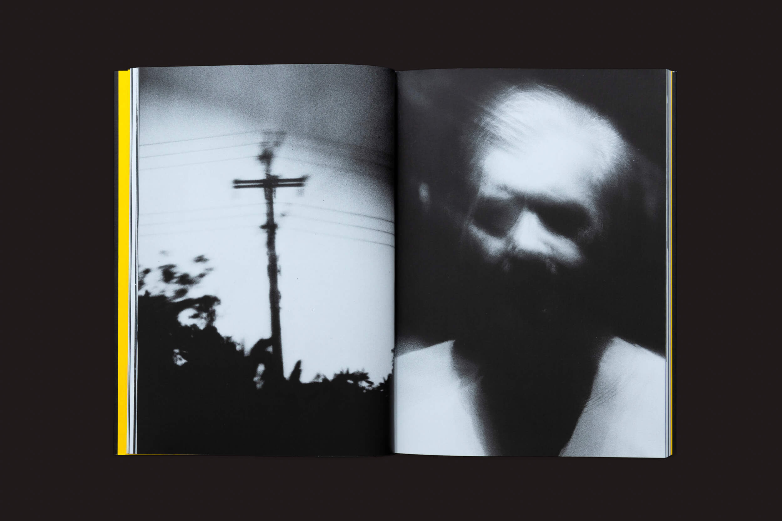 O livro Artur Lahoz: Klexos de Selo Turvo mostra uma silhueta na página esquerda de um poste telefônico e árvores sob nuvens, simbolizando klexos, e a página direita exibe uma pessoa borrada. O fundo escuro reflete o estilo distinto de Artur Lahoz.