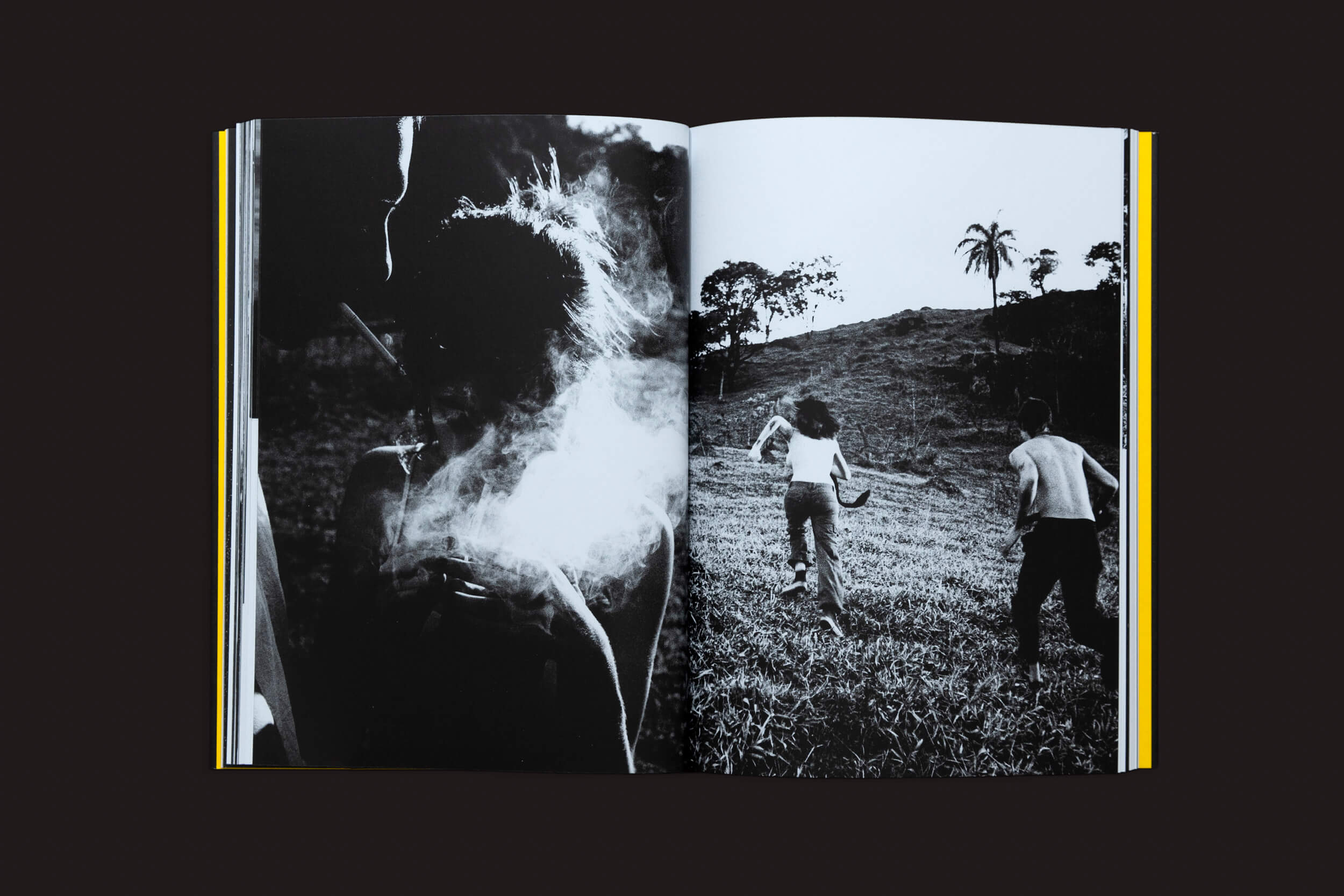 Uma cópia aberta de Artur Lahoz: Klexos de Selo Turvo exibe duas fotos em preto e branco. À esquerda, uma figura silhuetada envolta em fumaça incorpora klexos, enquanto à direita, dois indivíduos sobem uma colina gramada em direção a uma árvore solitária no horizonte, evocando memória.