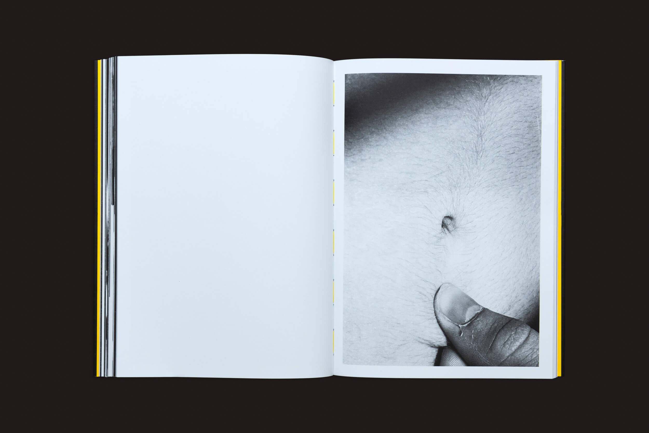 Um livro aberto intitulado Artur Lahoz: Klexos de Selo Turvo repousa sobre uma superfície escura. Sua página esquerda está em branco, e a direita exibe uma foto em preto e branco de um umbigo com um polegar ao lado — capturando um momento no tempo, refletindo a exploração da memória de Artur Lahoz por meio do Klexos.