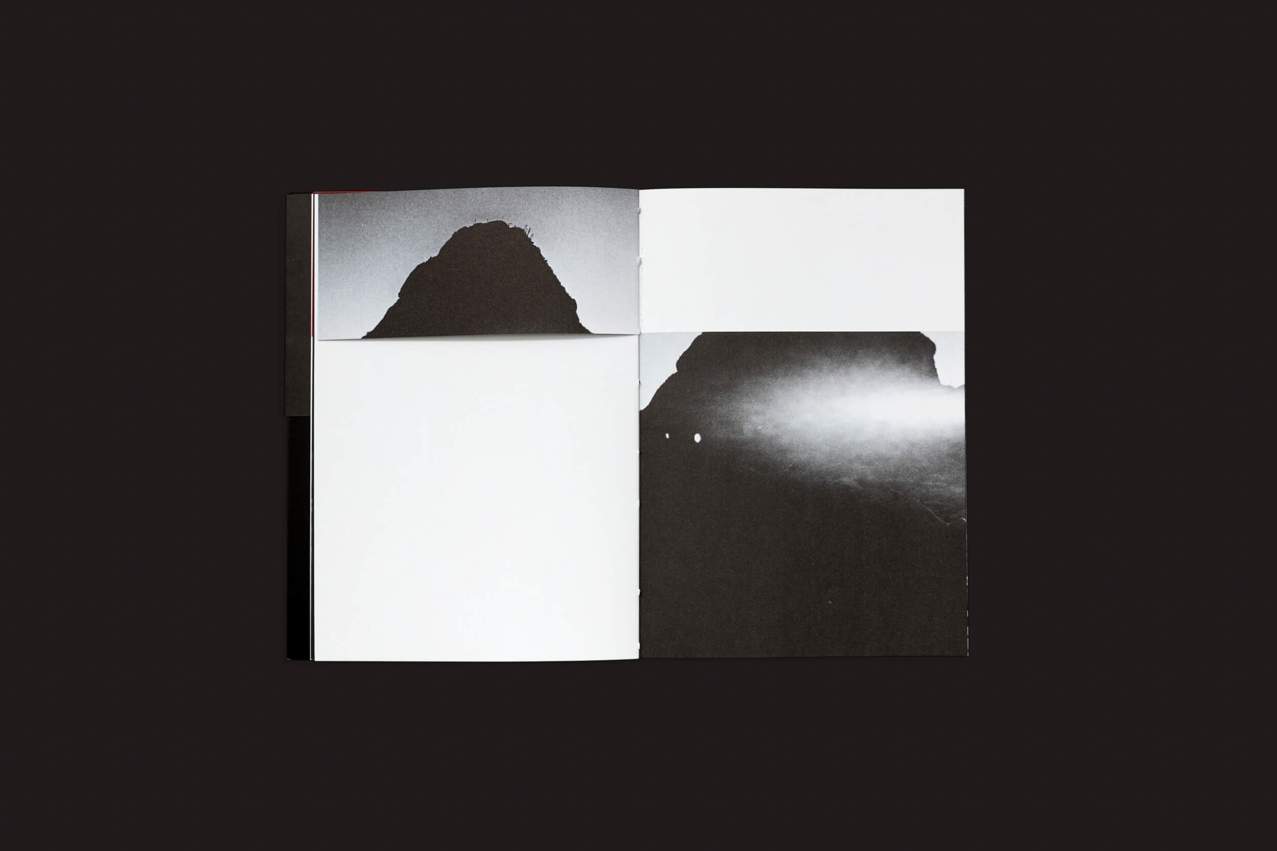 Em um fundo escuro, um livro aberto intitulado La herida del hombre, de Claudio Albarrán Briso, da SED Editorial, mostra imagens abstratas em preto e branco — a silhueta de uma montanha na página esquerda e sua gêmea banhada em luz brilhante na direita — sugerindo encontros simbólicos ou de herança masculina.