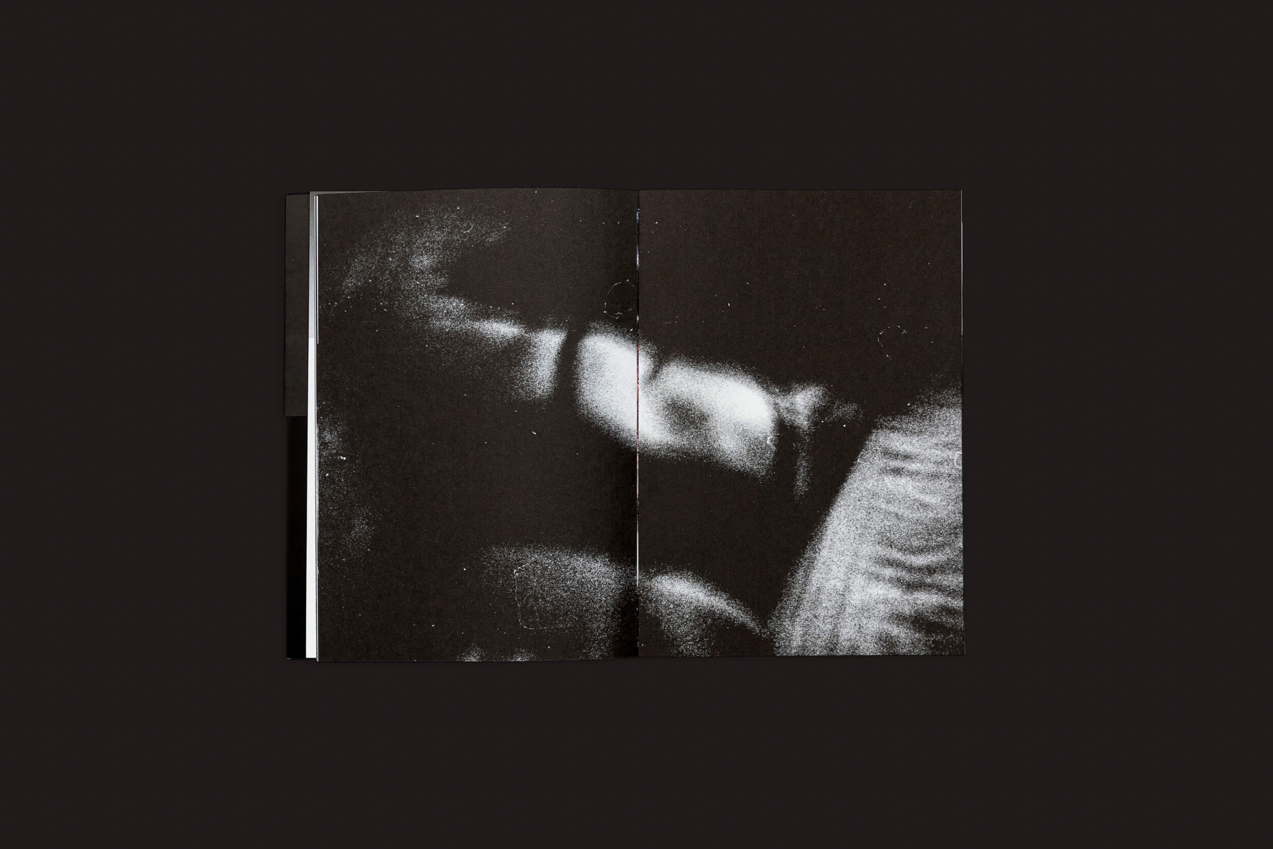 Um livro aberto revela uma imagem granulada e abstrata em preto e branco, com formas que lembram sombras e reflexos contra um fundo escuro, refletindo o fascínio misterioso de Claudio Albarrán Briso: La herida del hombre, da SED Editorial.