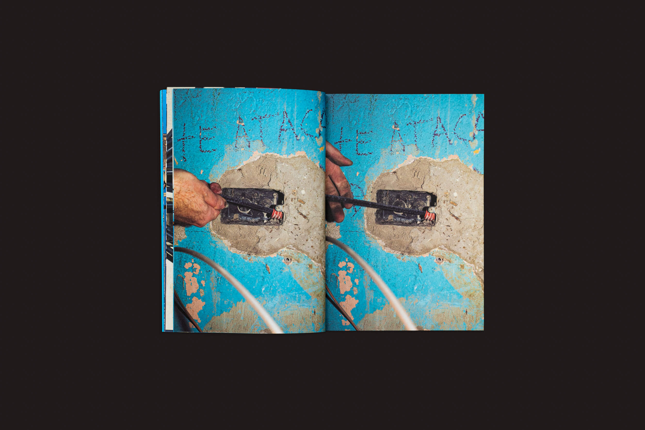 Um livro aberto de Henrik Malmström: NO da SED Editorial captura uma fotografia urbana vívida: mãos pintando uma parede de azul, revelando camadas texturizadas. Ferramentas sugerem reparo ou restauração em andamento, possivelmente com intervenções elétricas contra a paisagem urbana colorida.