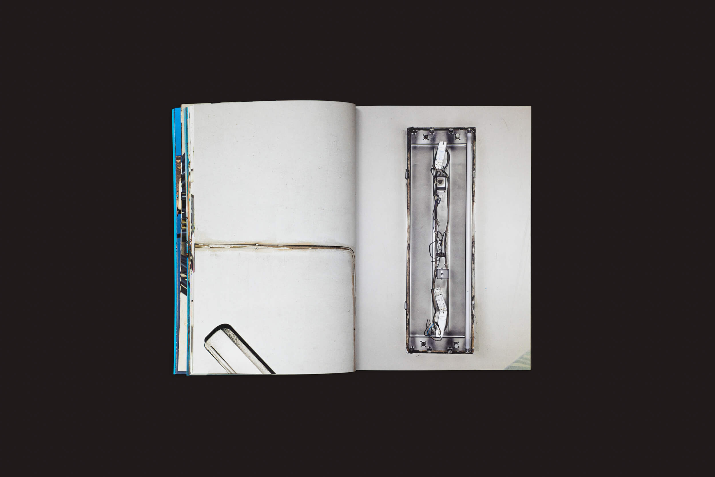 O livro Henrik Malmström: NO, da SED Editorial, está aberto sobre uma superfície escura, exibindo uma página com um edifício contra um céu azul e outra página com uma foto evocativa em preto e branco de instalações elétricas urbanas em metal.