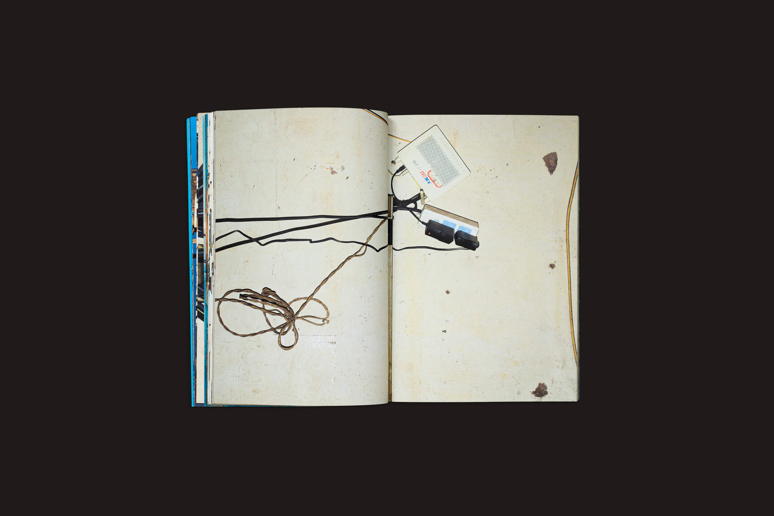 O NÃO de Henrik Malmström da SED Editorial está aberto sobre uma superfície escura, suas páginas gastas e envelhecidas com manchas. Perto, fones de ouvido descansam ao lado de um pequeno papel com esboços de instalações elétricas, adicionando uma vibração urbana.