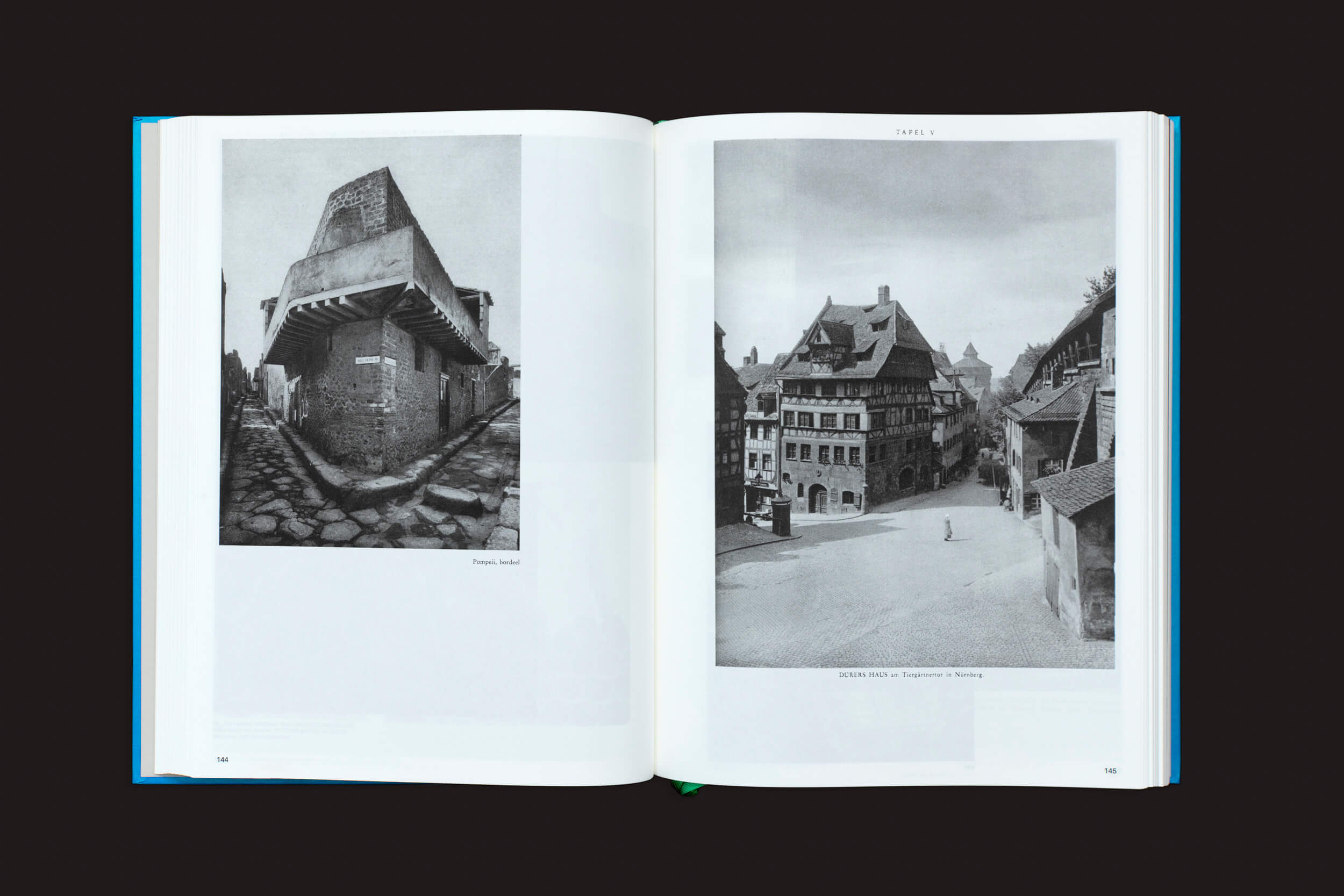 Um livro aberto de Batia Suter: Parallel Encyclopedia 1 da Roma Publications revela duas fotografias em preto e branco. A página da esquerda retrata um edifício com um telhado triangular, e a da direita apresenta uma vista da rua de Nuremberg, destacada por uma figura isolada na estrada.